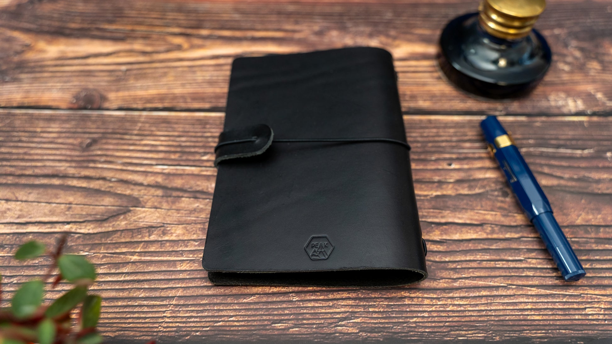 Black full grain vegetable tanned leather field notes sized cover with black elastic closure. Fits up to 2 field notes sized notebooks or 4 with connecting bands. Photo showing brand logo on the back at the bottom in the middle