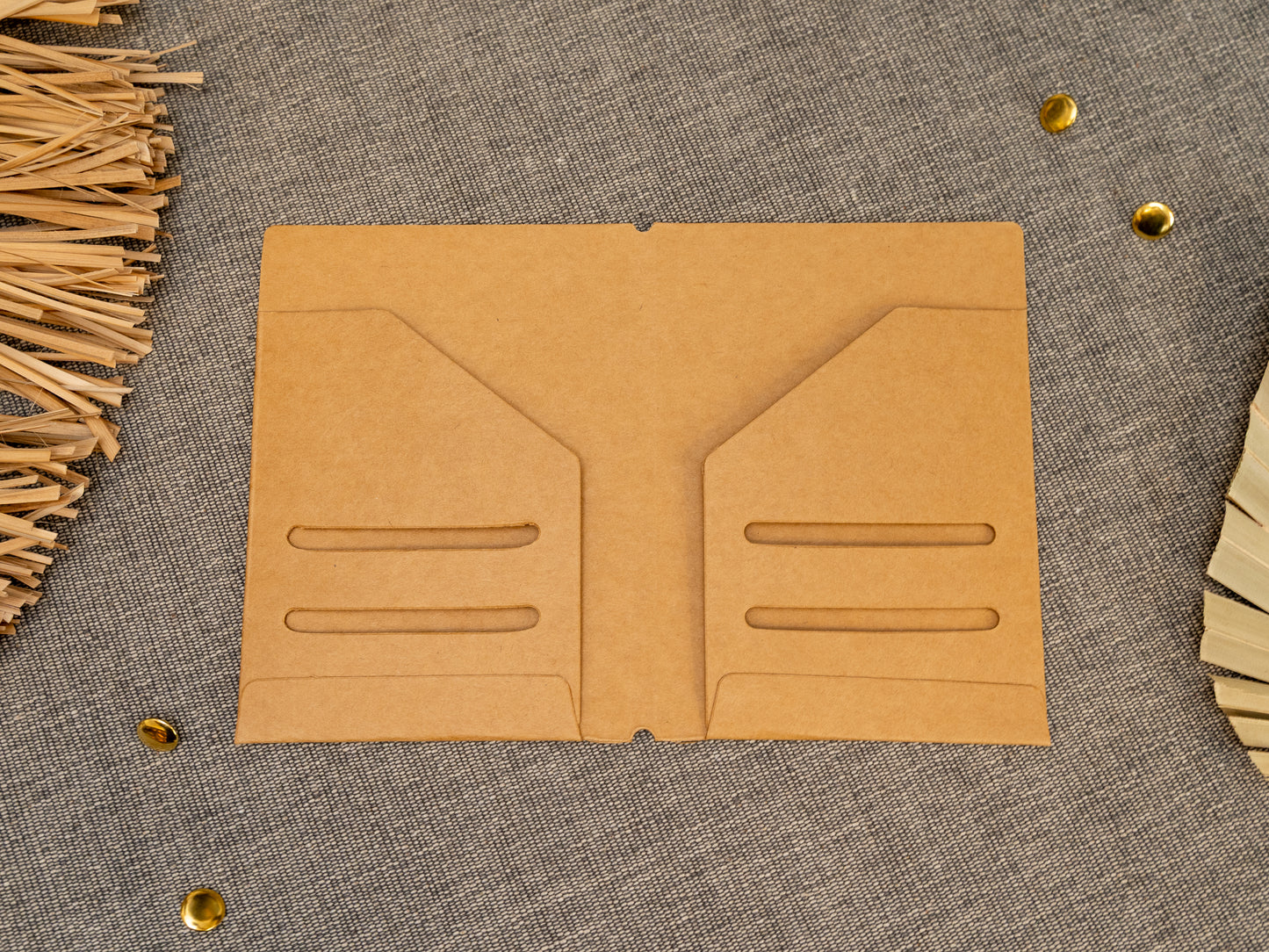 A tan kraft card TN notebook cover insert organizer in TN passport size, laid flat on a grey textured fabric surface with decorative dried leaves and small metal gold accents