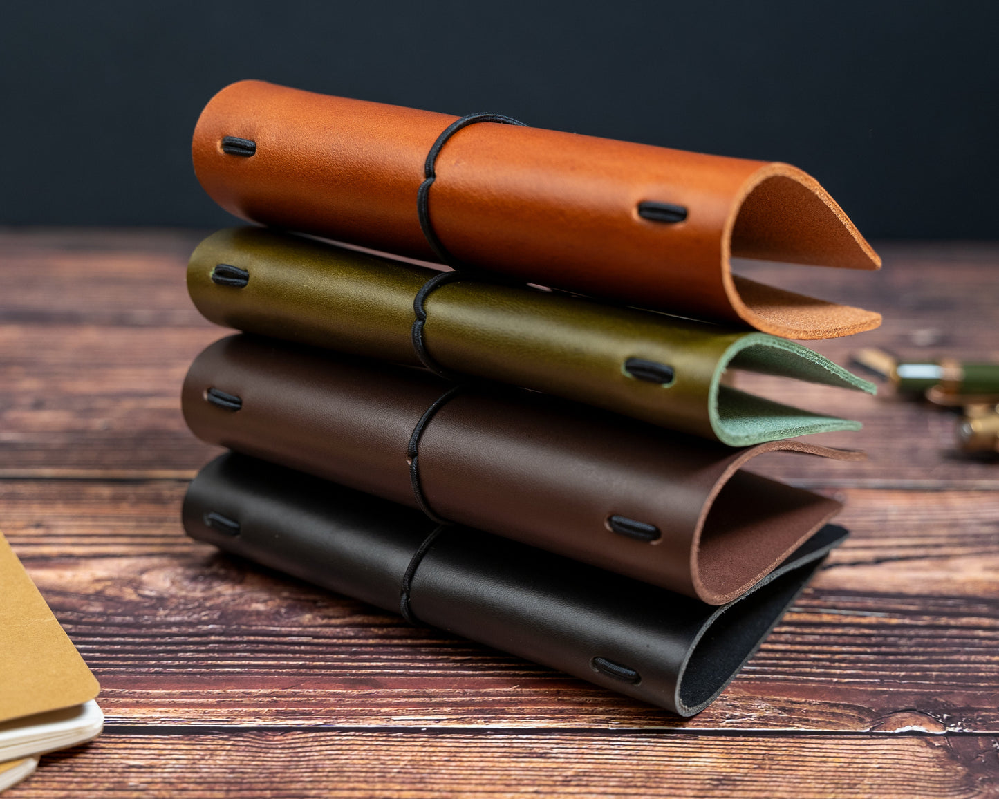 Stack of leather notebook covers in various colours on a wooden surface.