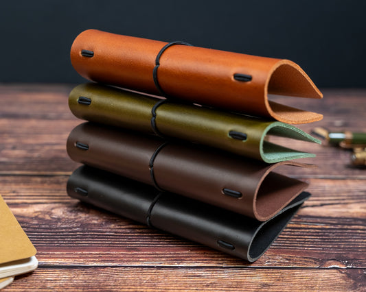 Stack of leather notebook covers in various colours on a wooden surface.