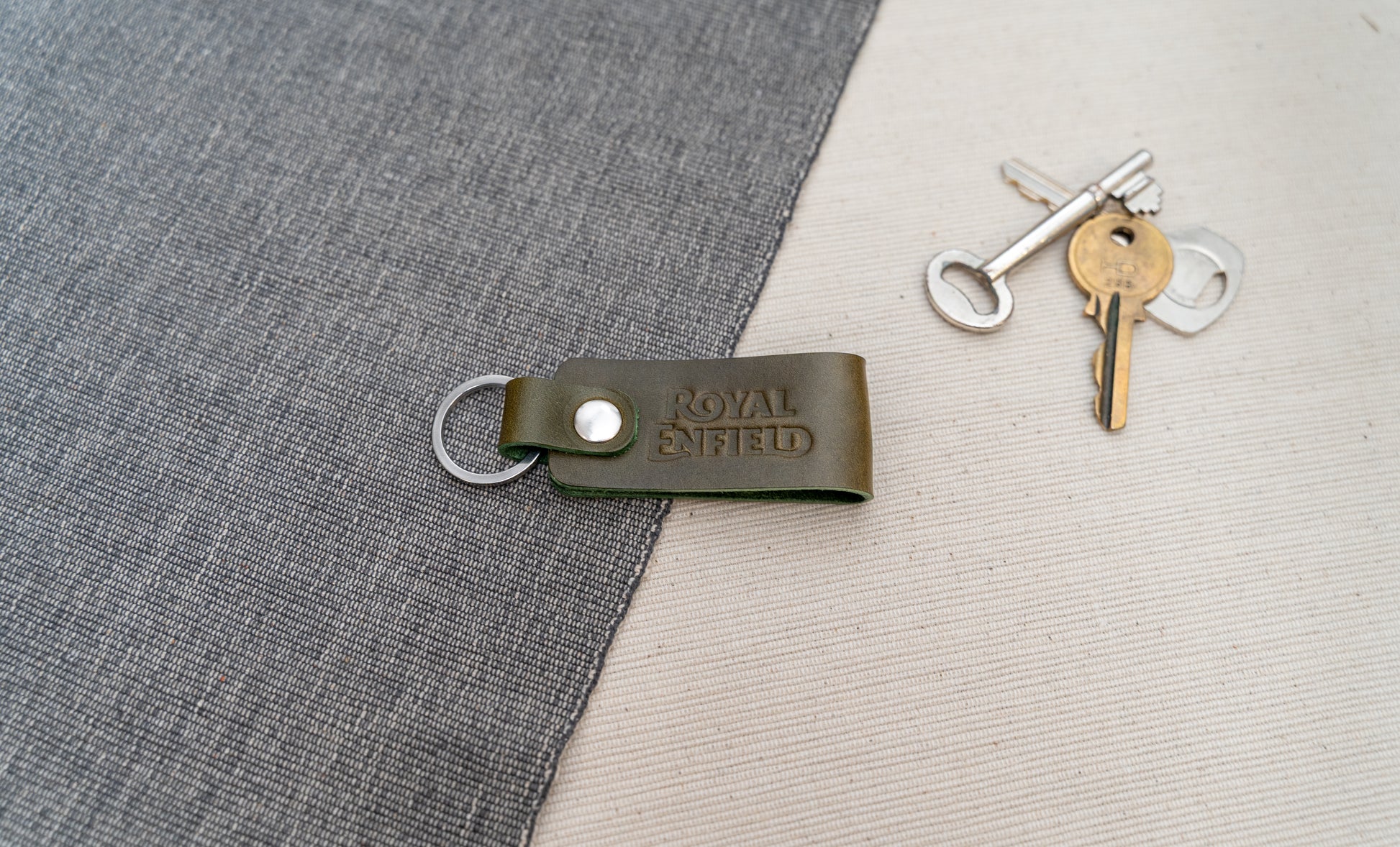 Olive Green Royal Enfield leather keychain on a textured surface with keys in the background.