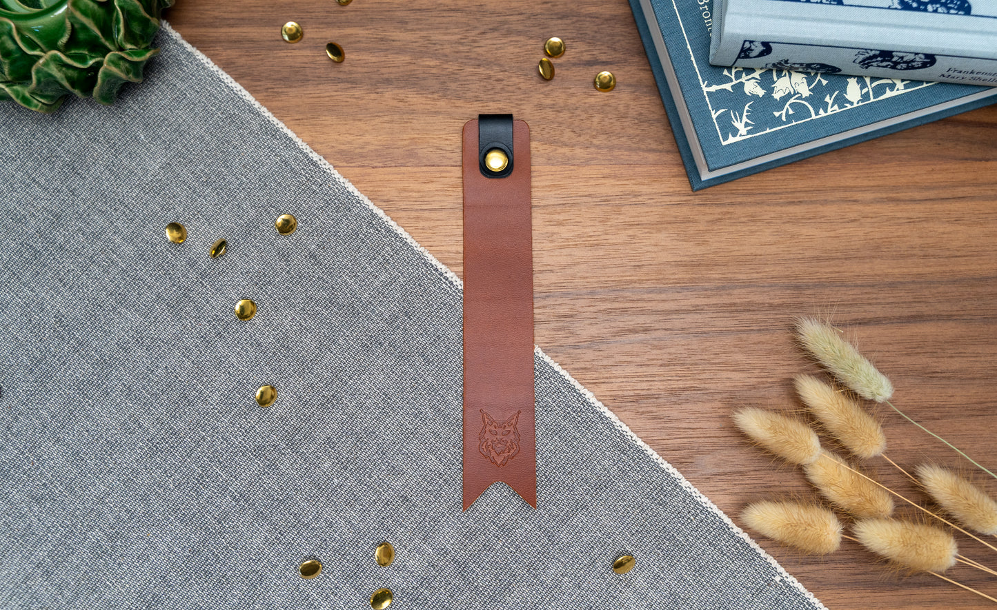 Leather bookmark in tan with a black tab folded over the top and a cut out at the bottom. Bookmark is debossed with an outline of a Maine Coon cats face. Stainless steel and brass rivets used to hold tab in place. Available in red, yellow, tan, olive green, purple, navy blue, dark brown, black with a choice of tab colour.