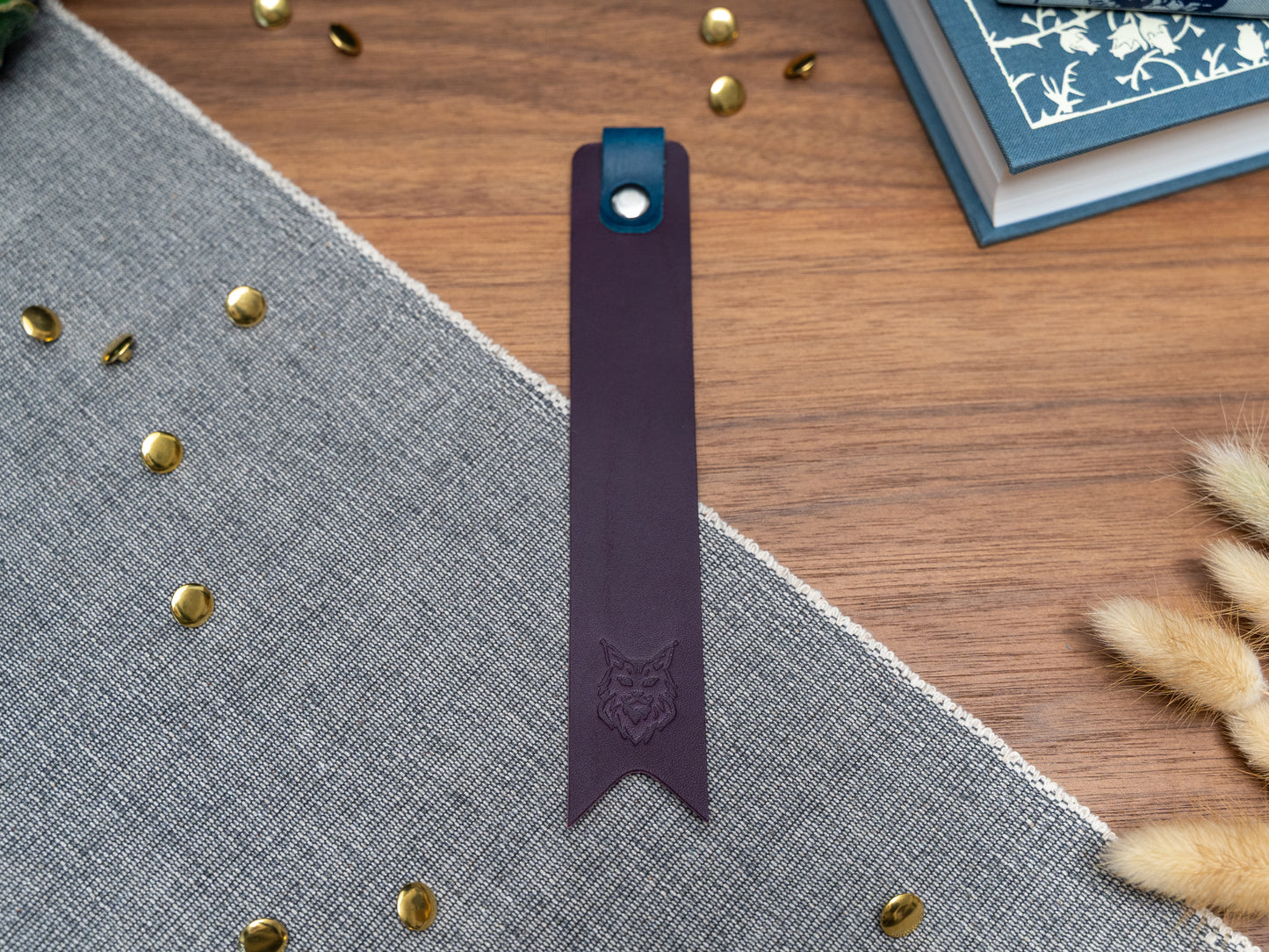 Leather bookmark in purple with a navy blue tab folded over the top and a cut out at the bottom. Bookmark is debossed with an outline of a Maine Coon cats face. Stainless steel and brass rivets used to hold tab in place. Available in red, yellow, tan, olive green, purple, navy blue, dark brown, black with a choice of tab colour.