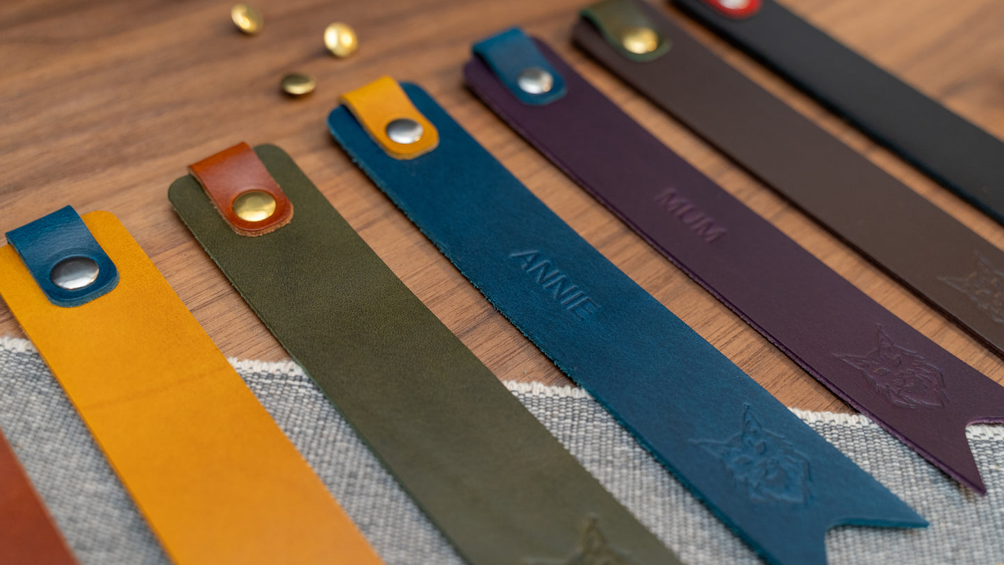 Leather bookmark in a selection of colours with folded tab over the top and a cut out at the bottom. Bookmark is debossed with an outline of a Maine Coon cats face. Stainless steel and brass rivets used to hold tab in place. Available in red, yellow, tan, olive green, purple, navy blue, dark brown, black with a choice of tab colour.