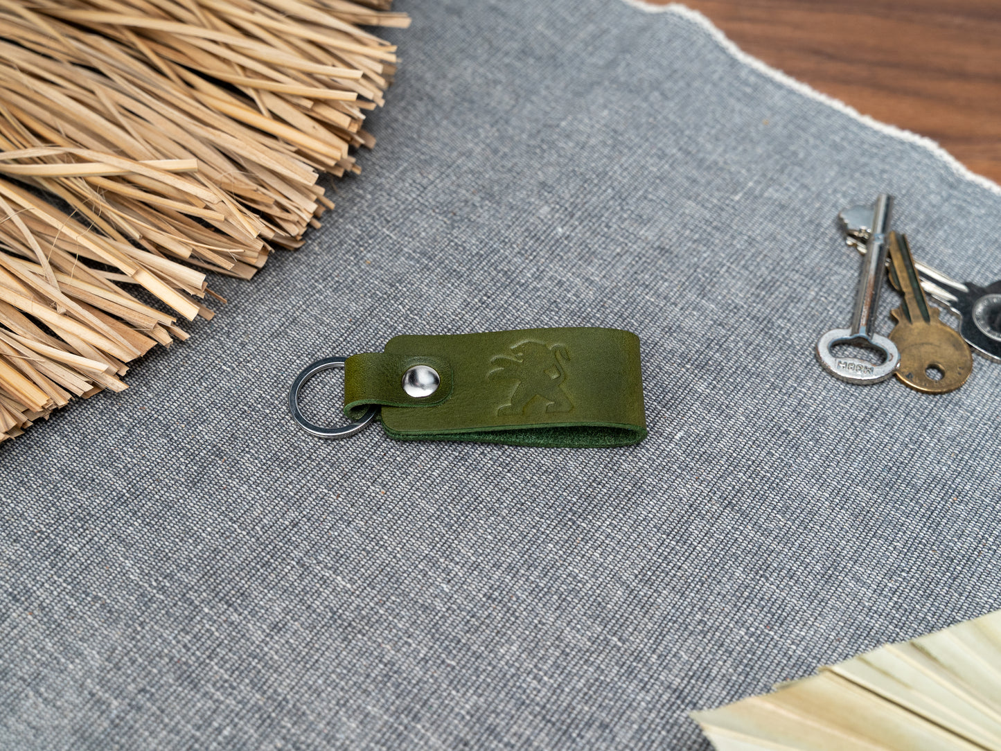 Folded olive green leather keyring with the Peugeot car logo debossed on it. Made from Italian full grain leather