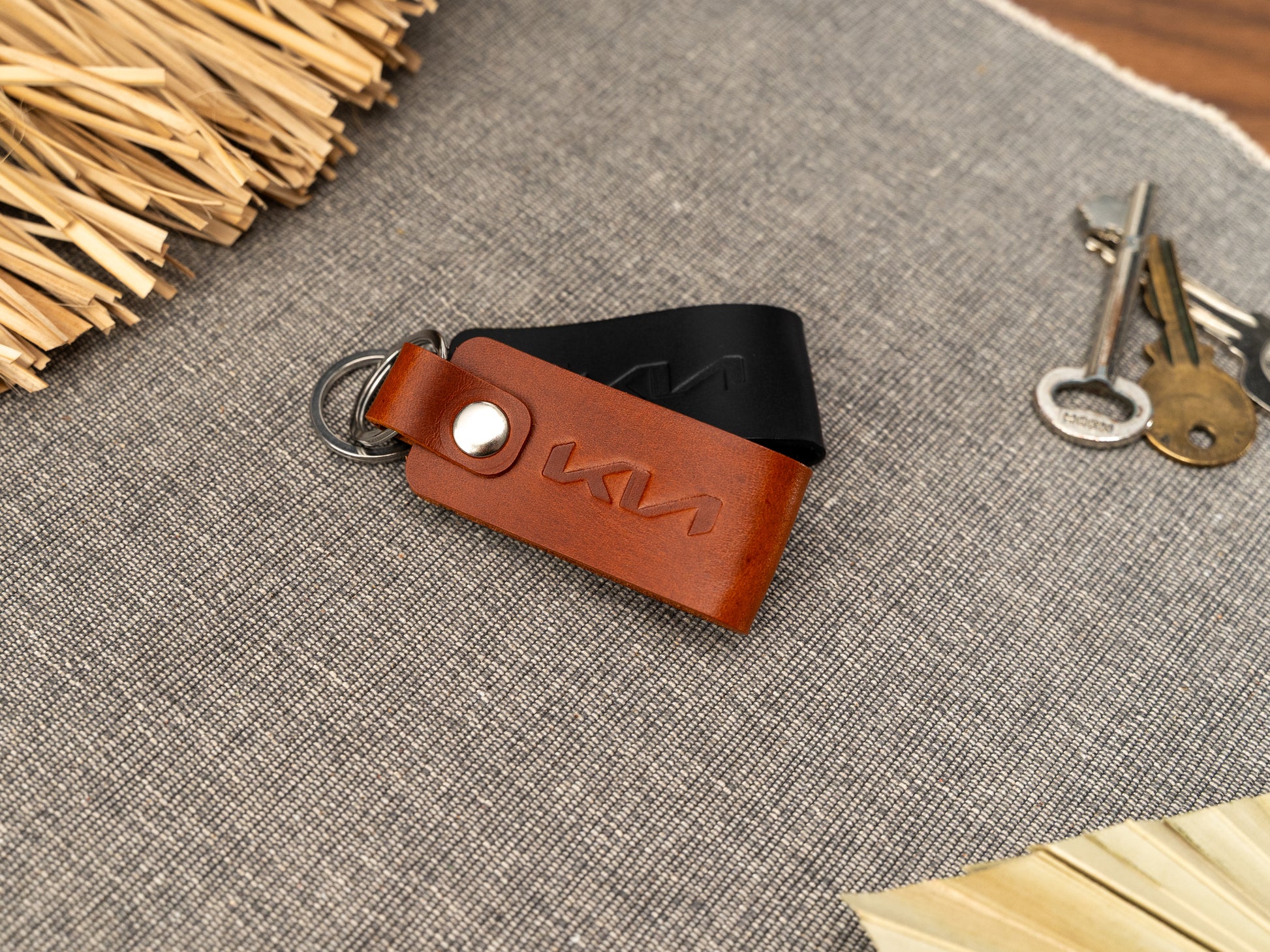 Folded tan and black leather keyrings/keychains with the Kia car logo debossed on them. Made from full grain leather with stainless steel split ring and rivet.