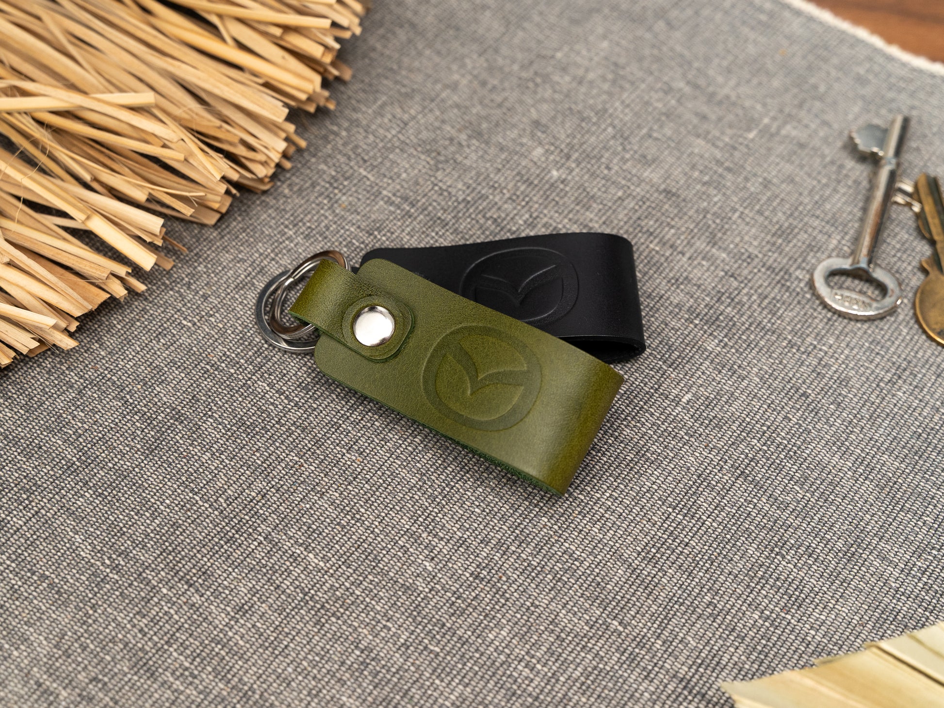 Folded olive green and black leather keyrings/keychains with the Mazda car logo debossed on them. Made from full grain leather with stainless steel split ring and rivet.