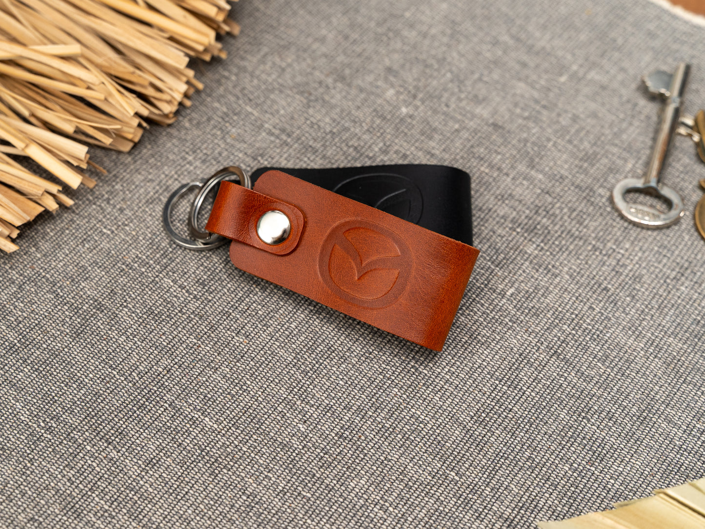 Folded tan and black leather keyrings/keychains with the Mazda car logo debossed on them. Made from full grain leather with stainless steel split ring and rivet.