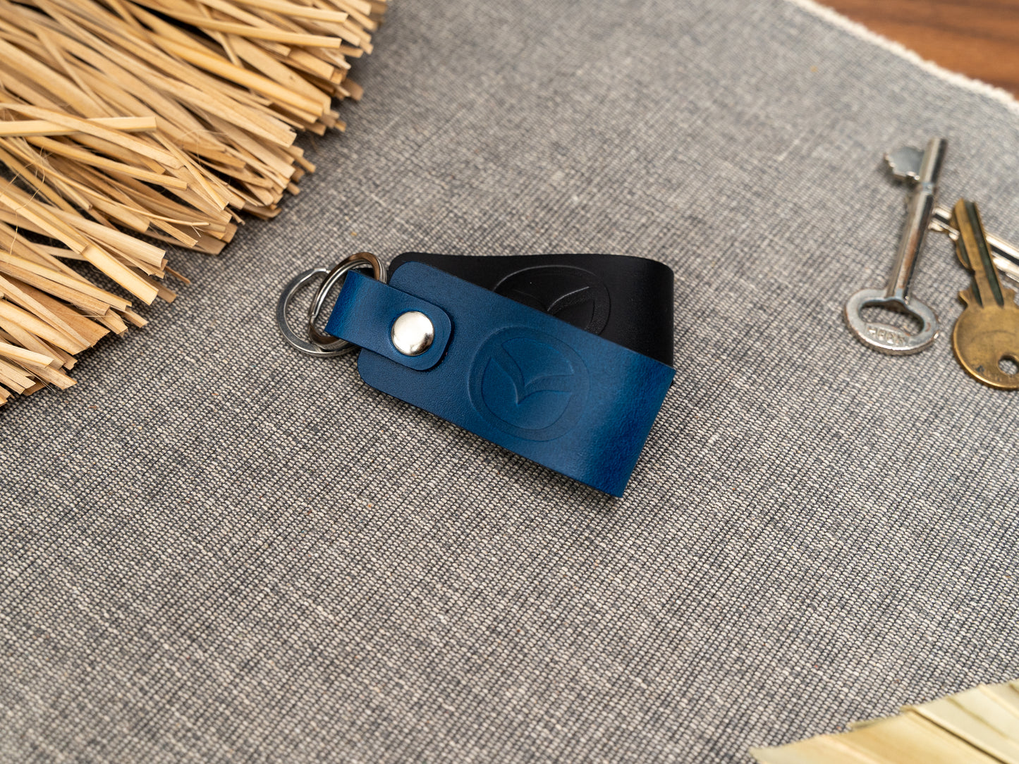 Folded navy blue and black leather keyrings/keychains with the Mazda car logo debossed on them. Made from full grain leather with stainless steel split ring and rivet.