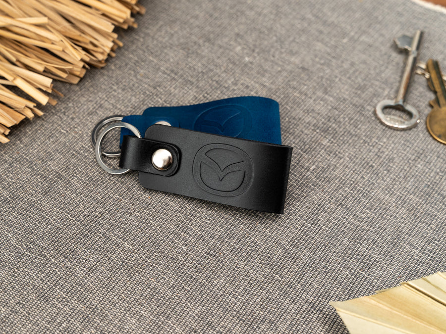 Folded black and navy blue leather keyrings/keychains with the Mazda car logo debossed on them. Made from full grain leather with stainless steel split ring and rivet.