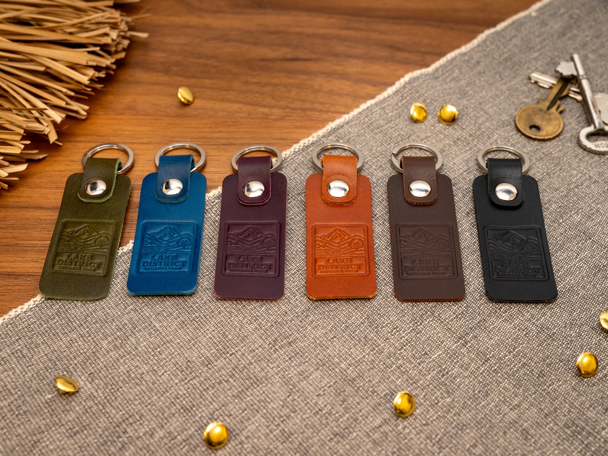 Several leather keyrings with a rectangular design in various colours such as olive green, navy blue, purple, tan, dark brown and black keyrings/keychains embossed with an image of the lake district. Stainless steel split ring and rivet.