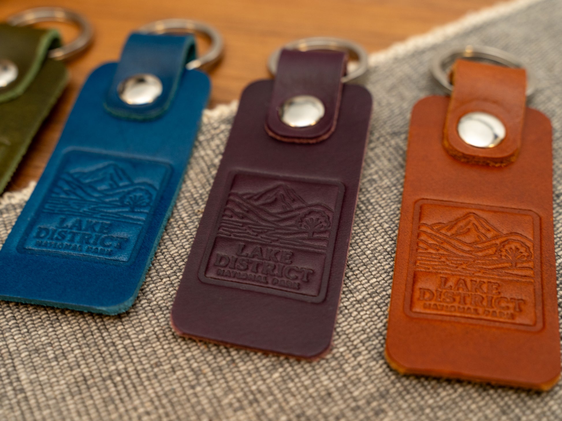 Several leather keyrings with a rectangular design in various colours such as navy blue, purple and tan keyrings/keychains embossed with an image of the lake district. Stainless steel split ring and rivet.