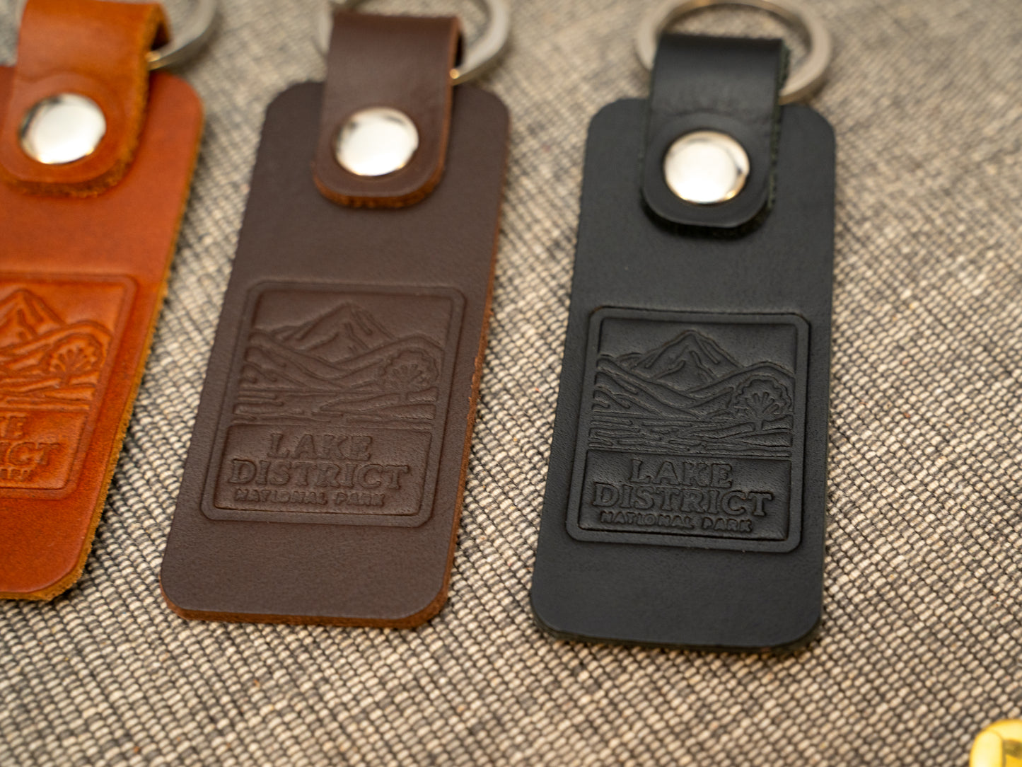 Several keyrings with a rectangular design in various colours such as tan, dark brown and black keyrings/keychains embossed with an image of the lake district. Stainless steel split ring and rivet.