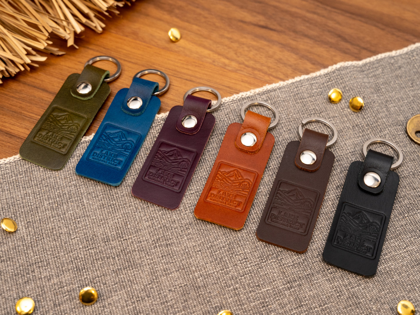 Several leather keyrings with a rectangular design in various colours such as olive green, navy blue, purple, tan, dark brown and black keyrings/keychains embossed with an image of the lake district. Stainless steel split ring and rivet.