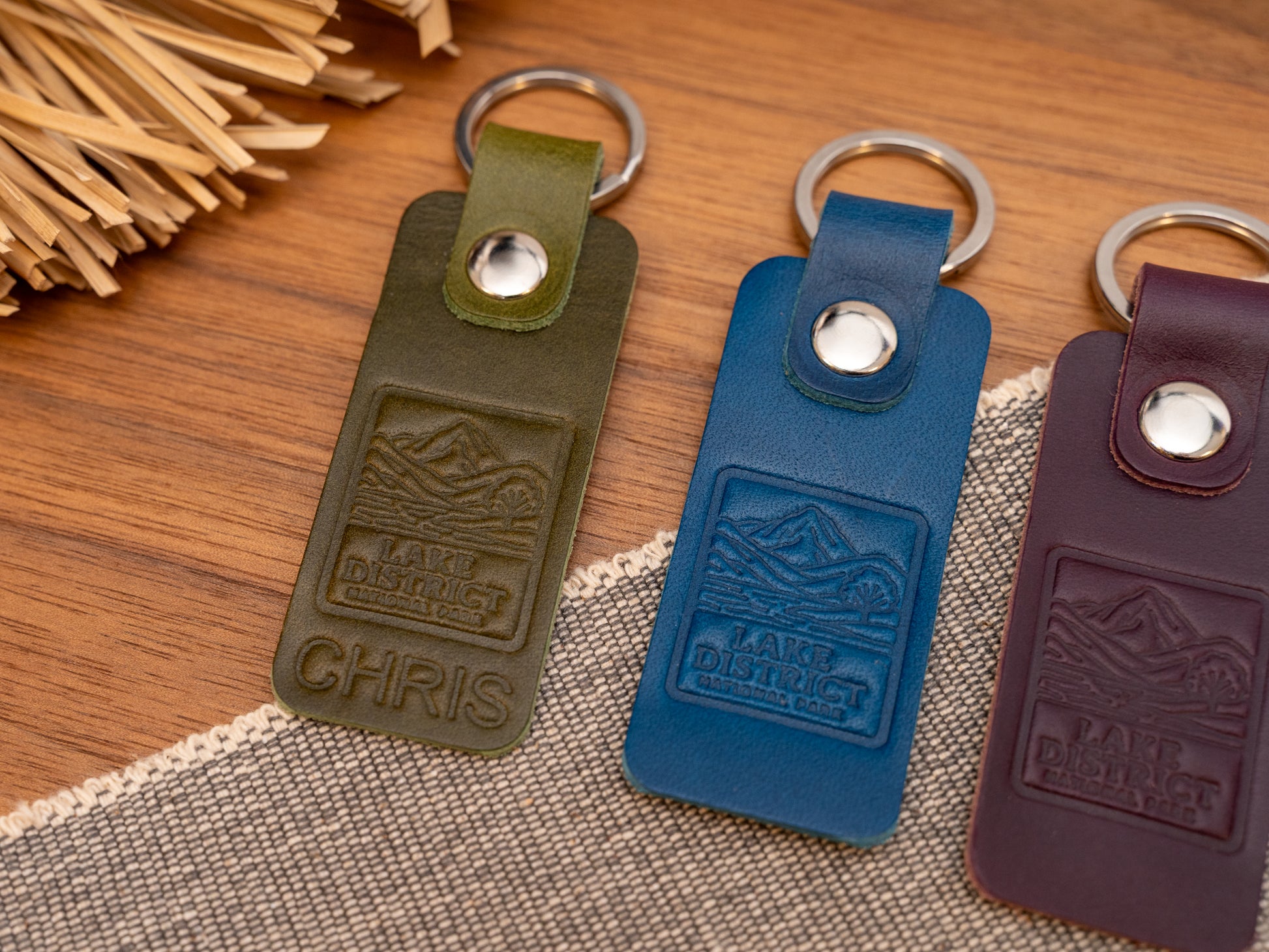 Several leather keyrings with a rectangular design in various colours such as olive green, navy blue and purple keyrings/keychains embossed with an image of the lake district. Stainless steel split ring and rivet.