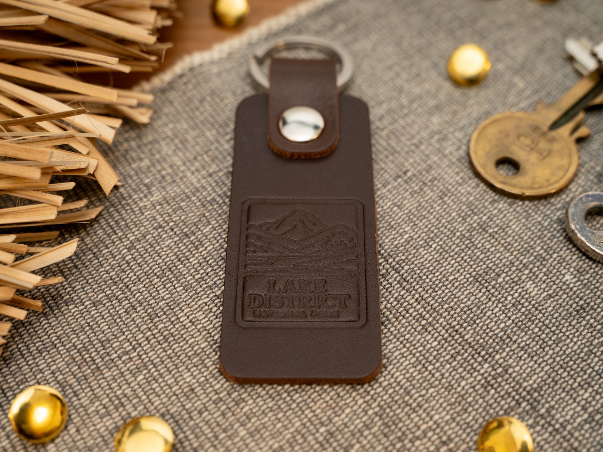 A leather keyring with a rectangular design in dark brown. Keyring/keychain is debossed with an image of the lake district. Stainless steel split ring and rivet.