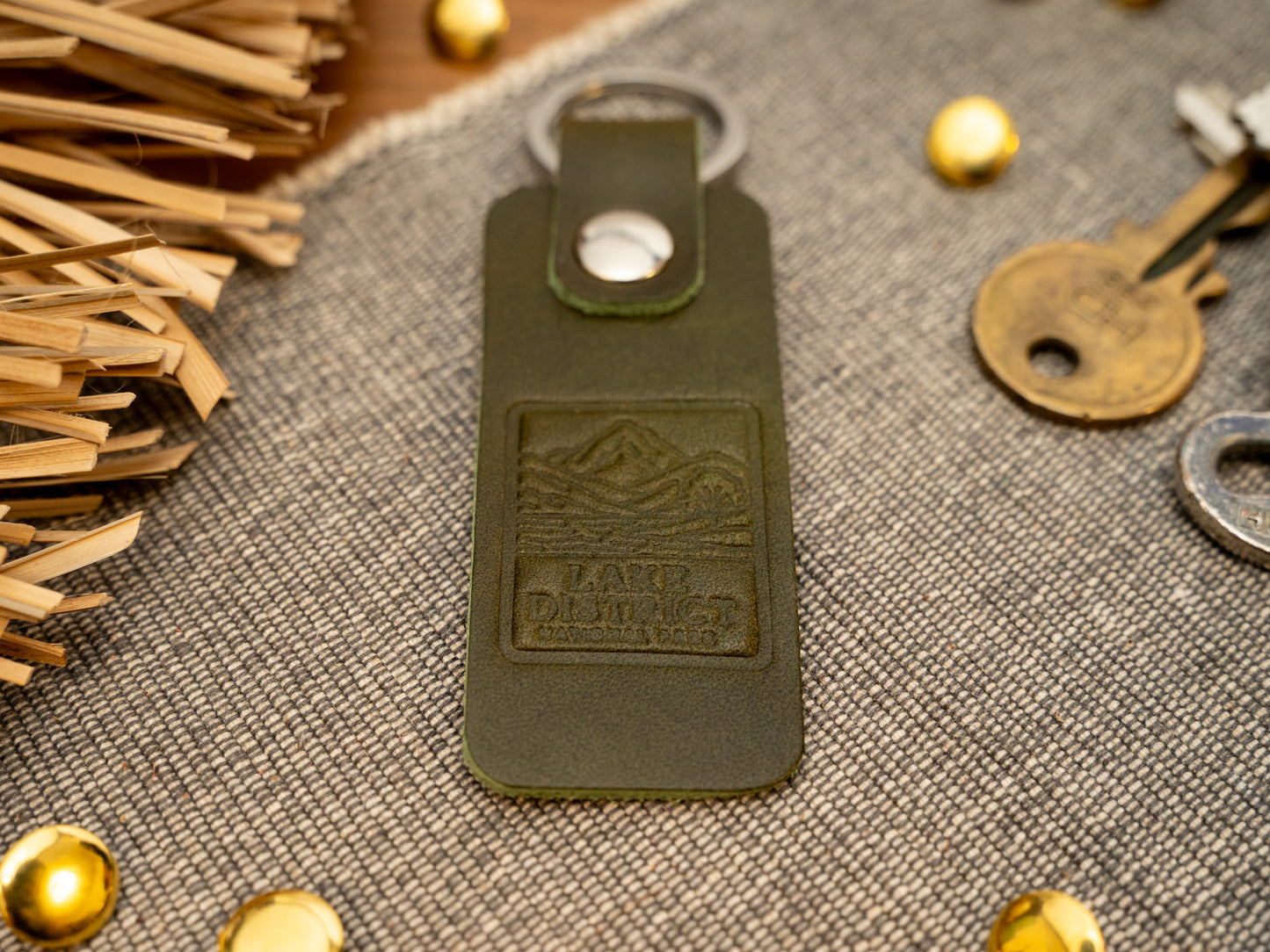 A leather keyring with a rectangular design in olive green. Keyring/keychain is debossed with an image of the lake district. Stainless steel split ring and rivet.
