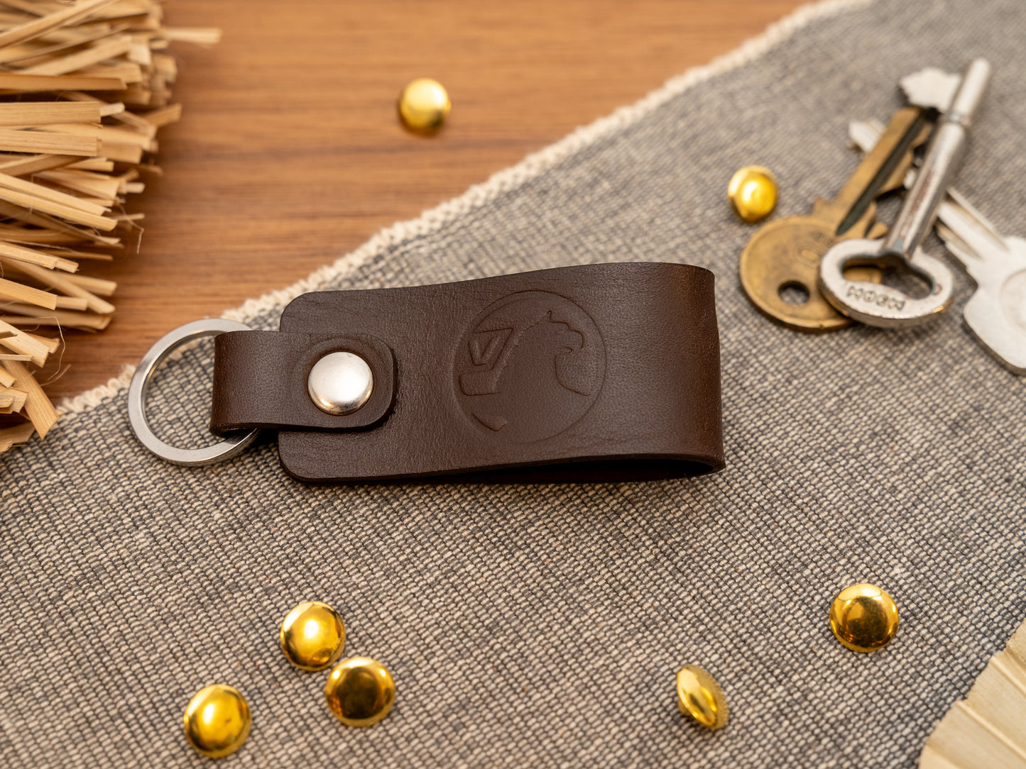 Folded dark brown leather keyring/keychain with the Vauxhall car logo debossed on it. Made from full grain leather with stainless steel split ring and rivet.