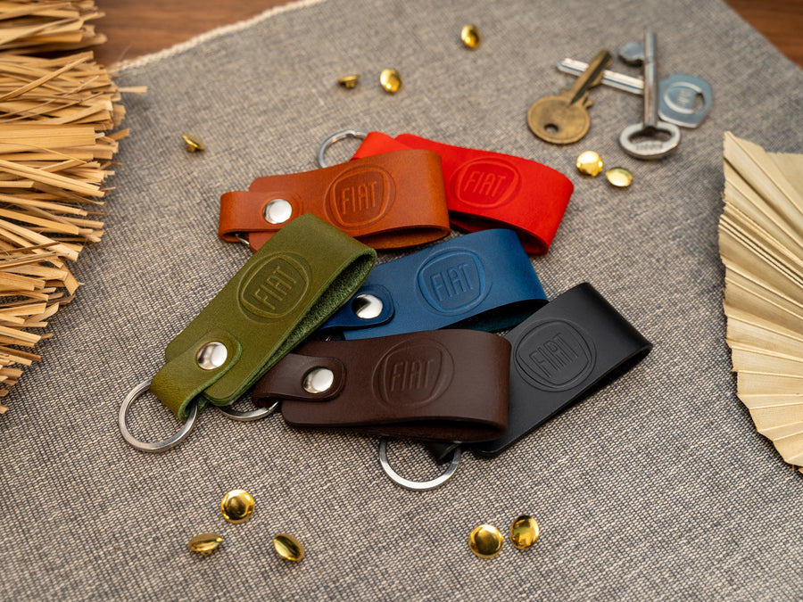 Several keyrings with a folded design in various colours such as tan, olive green, navy blue, dark brown, black and red keyrings/keychains embossed with the Fiat car logo. Stainless steel split ring and rivet.