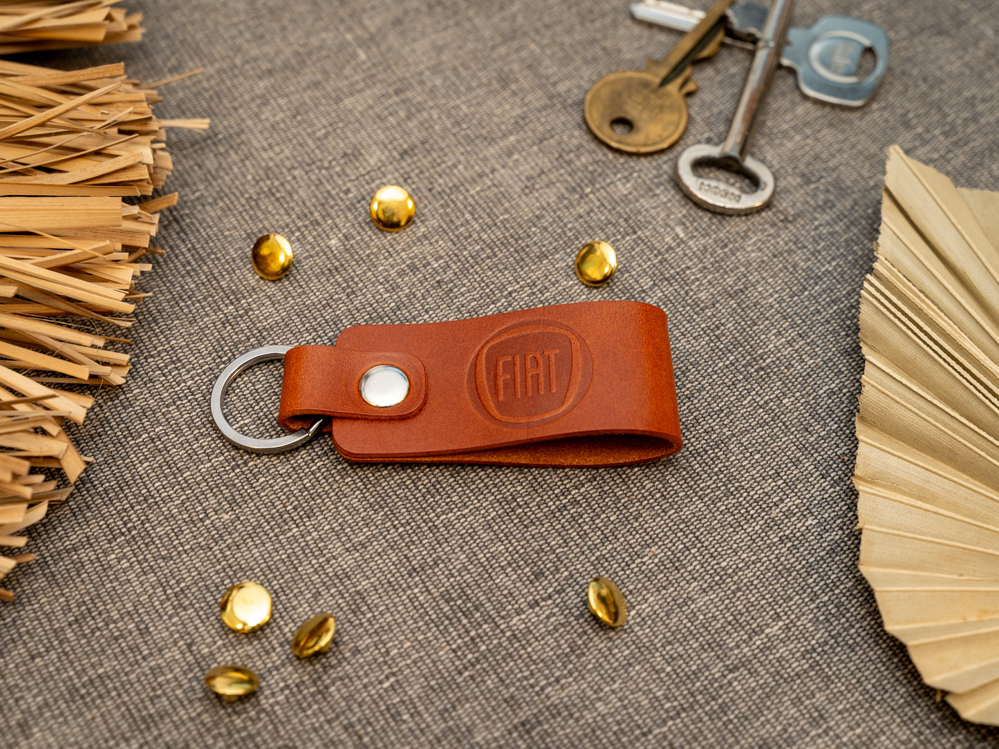 Keyring with a folded design in tan. The keychain has been embossed with the Fiat car logo. Stainless steel split ring and rivet.