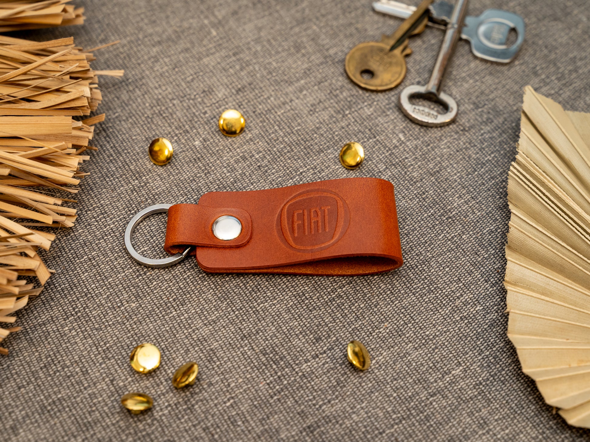 Keyring with a folded design in tan. The keychain has been embossed with the Fiat car logo. Stainless steel split ring and rivet.