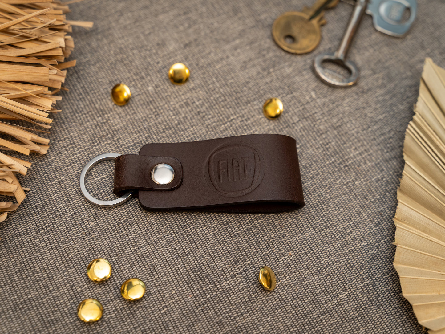 Brown leather keychain with Fiat logo on a textured surface with keys and decorative elements.