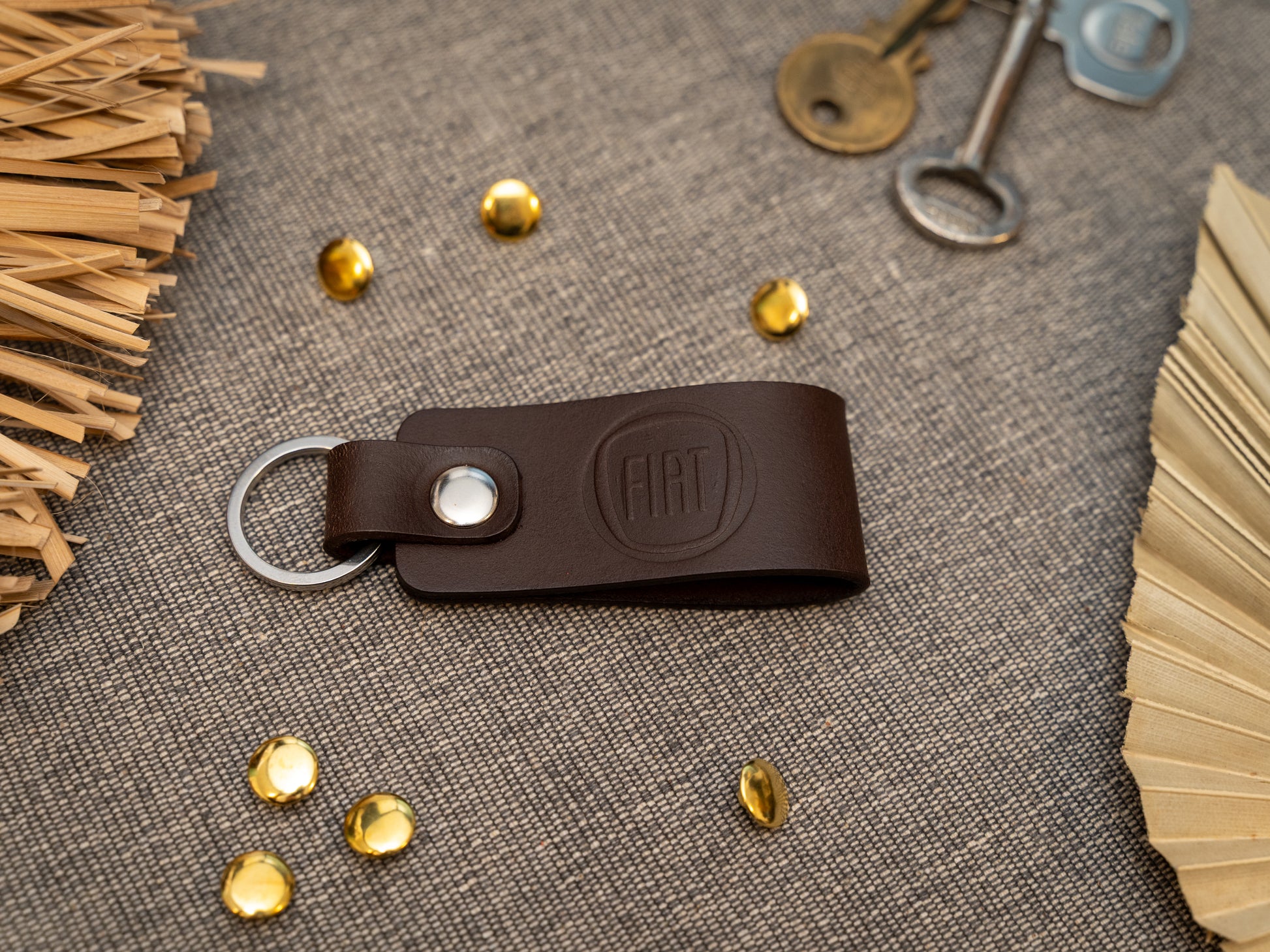 Brown leather keychain with Fiat logo on a textured surface with keys and decorative elements.