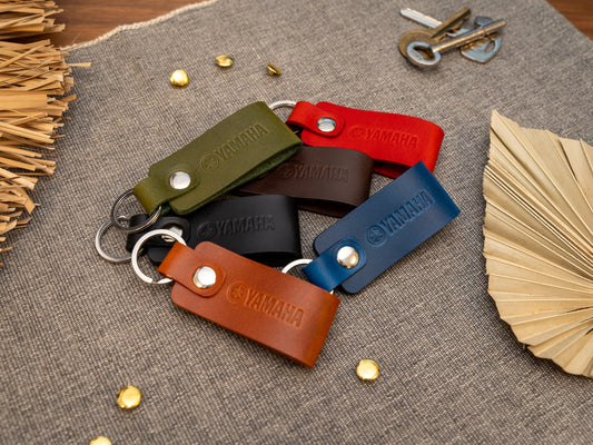 Several keyrings with a folded design in various colours such as tan, olive green, navy blue, dark brown, black and red keyrings/keychains embossed with the Yamaha motorbike logo. Stainless steel split ring and rivet.