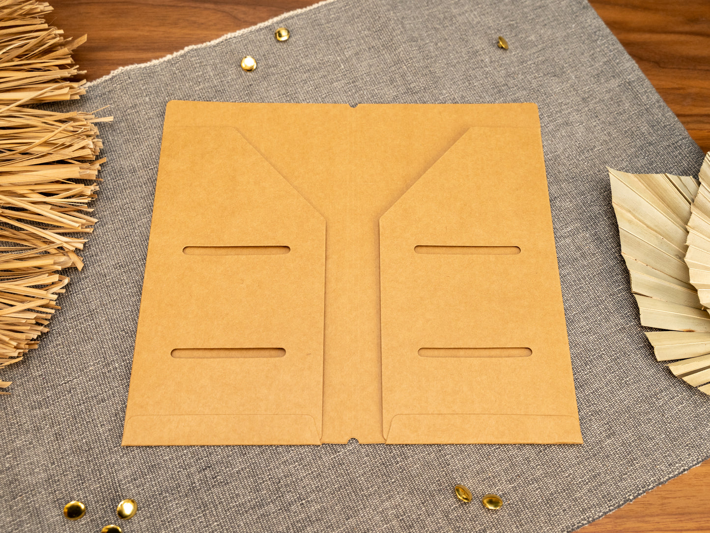 A tan kraft card TN notebook cover insert organizer in TN standard size, laid flat on a grey textured fabric surface with decorative dried leaves and small metal gold accents