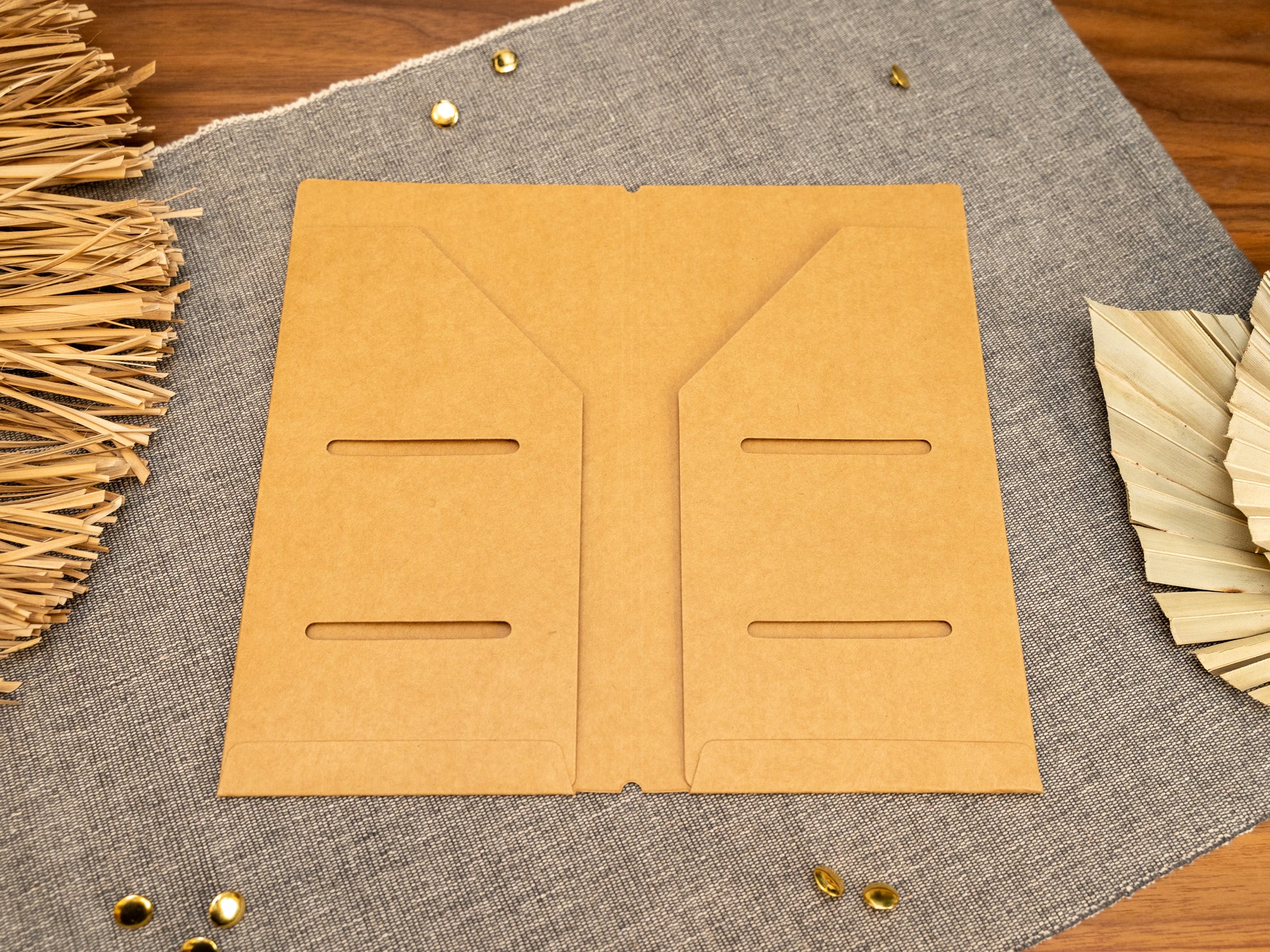A tan kraft card TN notebook cover insert organizer in TN standard size, laid flat on a grey textured fabric surface with decorative dried leaves and small metal gold accents