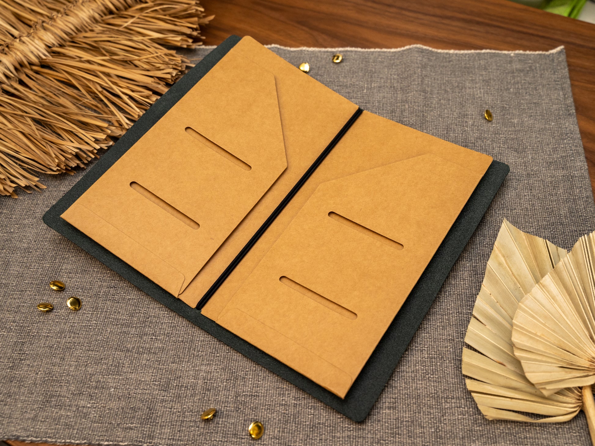 An open tn standard size Kraft card document holder or organizer in a leather notebook cover, shown on a textured gray fabric surface with decorative dried leaves and small gold accents.