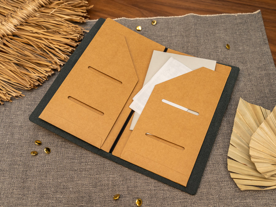 An open tn standard size Kraft card document holder or organizer in a leather notebook cover, shown on a textured gray fabric surface with decorative dried leaves and small gold accents.