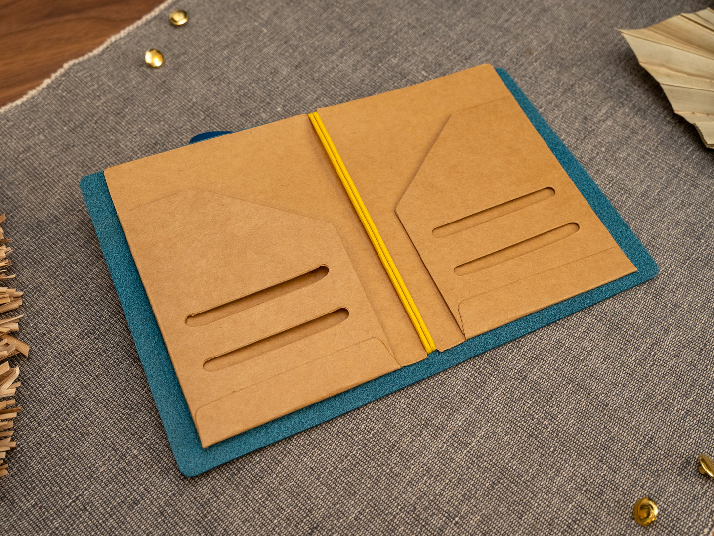 An open tn passport size Kraft card document holder or organizer in a leather notebook cover, shown on a textured gray fabric surface with decorative dried leaves and small gold accents.