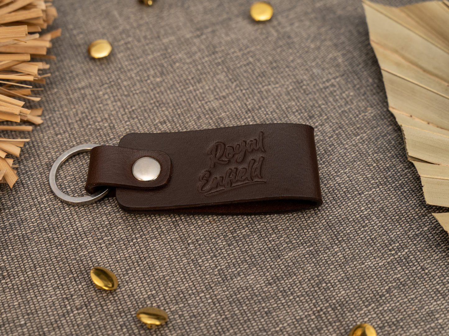 Folded dark brown leather keyring/keychain with Royal Enfield in a cursive style font debossed on it. Made from full grain leather with stainless steel split ring and rivet.