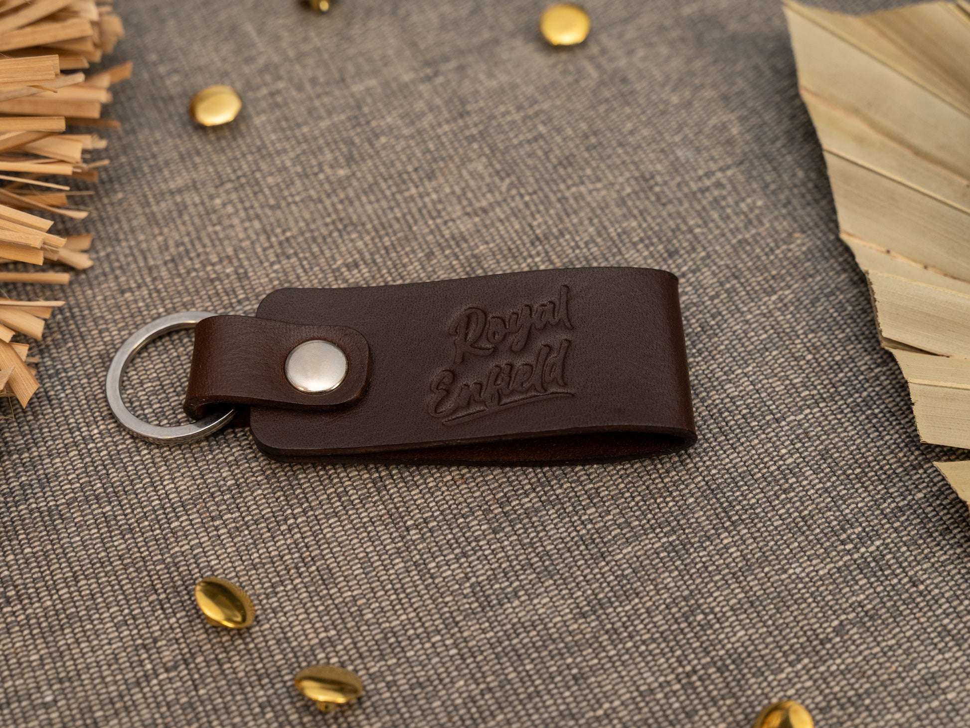 Folded dark brown leather keyring/keychain with Royal Enfield in a cursive style font debossed on it. Made from full grain leather with stainless steel split ring and rivet.
