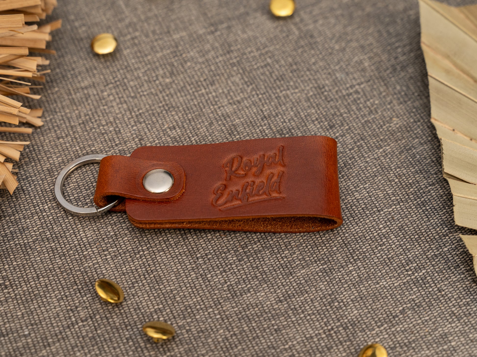 Folded tan leather keyring/keychain with Royal Enfield in a cursive style font debossed on it. Made from full grain leather with stainless steel split ring and rivet.
