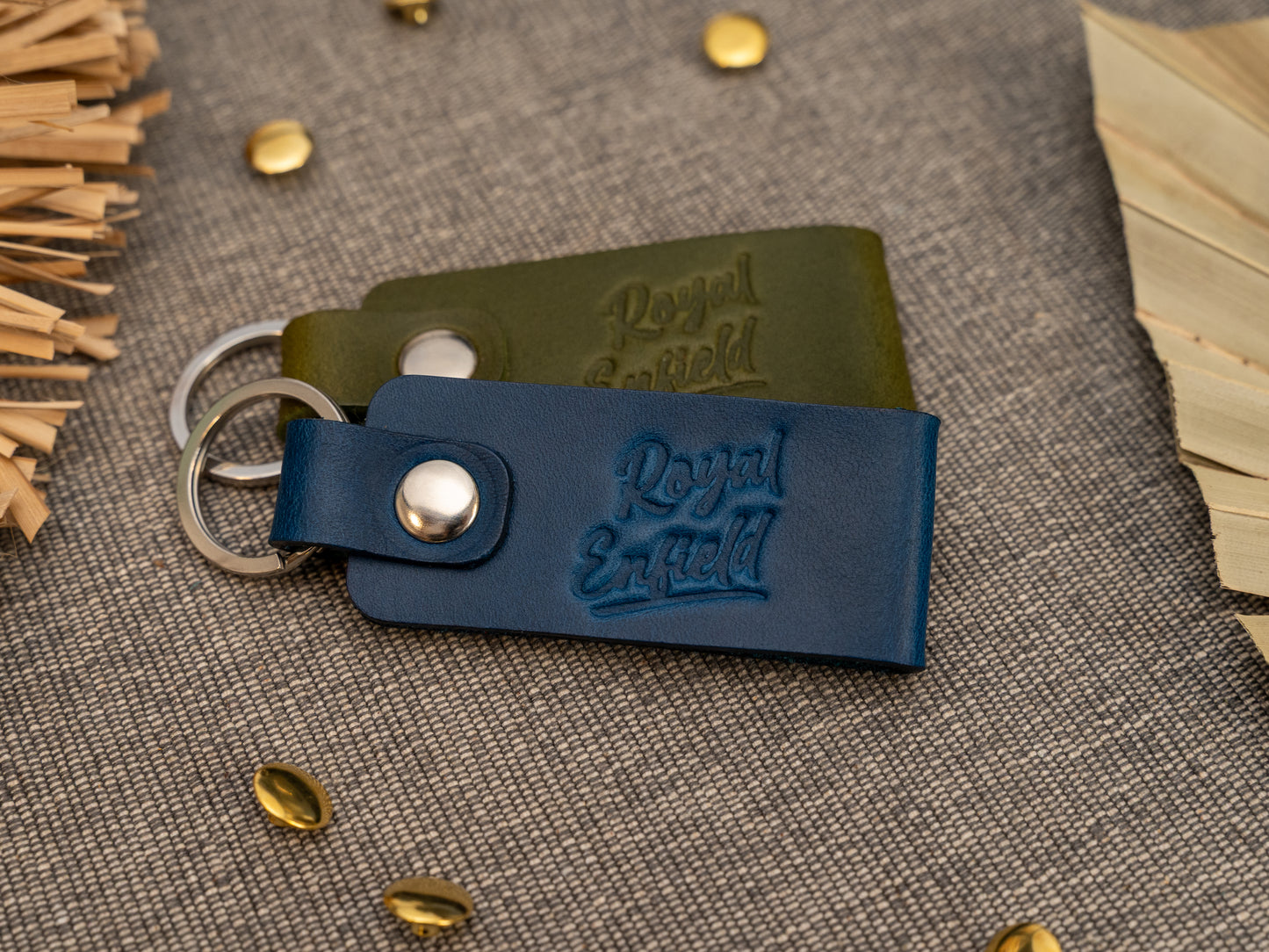 Folded navy blue and olive green leather keyrings/keychains with Royal Enfield in a cursive style font debossed on them. Made from full grain leather with stainless steel split ring and rivet.
