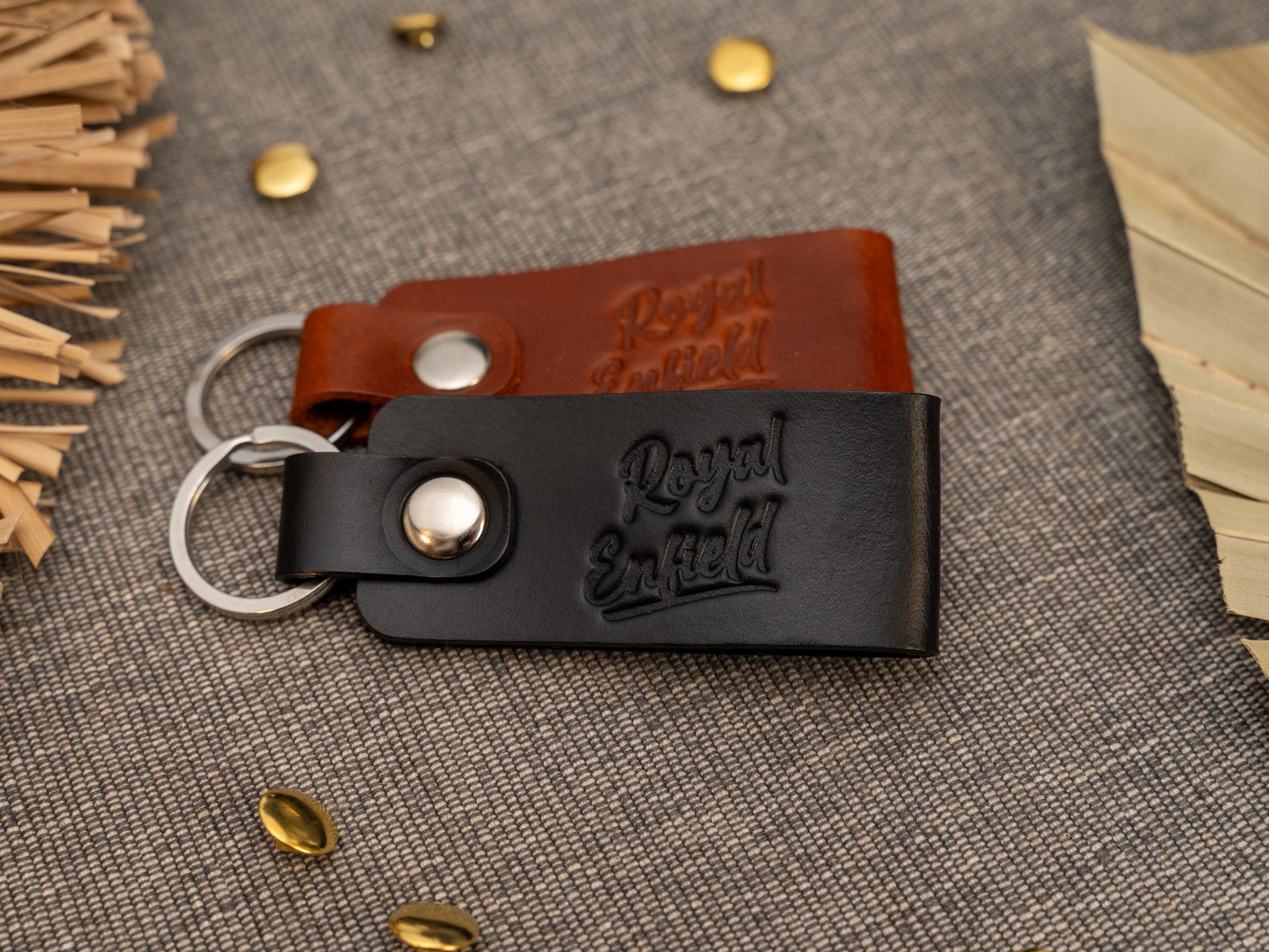 Folded black and tan leather keyrings/keychains with Royal Enfield in a cursive style font debossed on them. Made from full grain leather with stainless steel split ring and rivet.