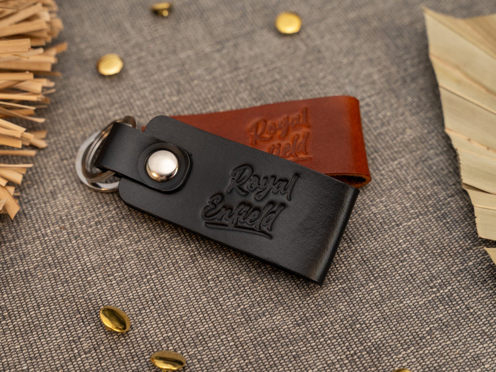 Folded black and tan green leather keyrings/keychains with Royal Enfield in a cursive style font debossed on them. Made from full grain leather with stainless steel split ring and rivet.