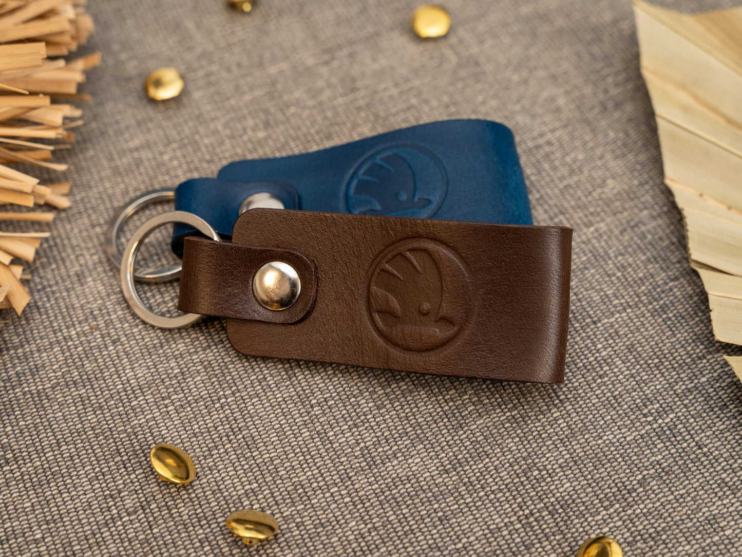 Keyrings with a folded design in dark brown and navy blue. The keychain has been embossed with the Skoda car logo. Stainless steel split ring and rivet.
