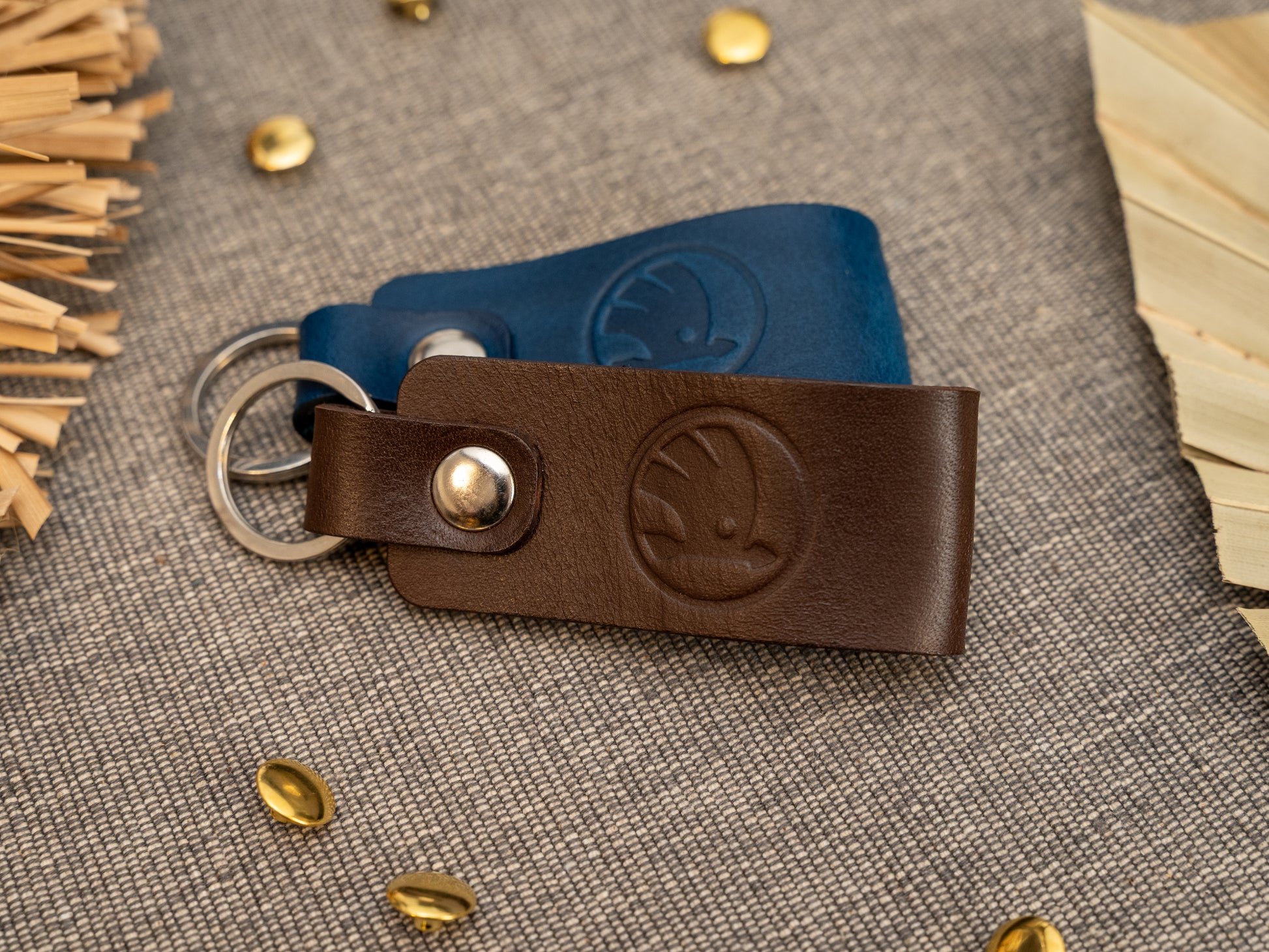 Keyrings with a folded design in dark brown and navy blue. The keychain has been embossed with the Skoda car logo. Stainless steel split ring and rivet.
