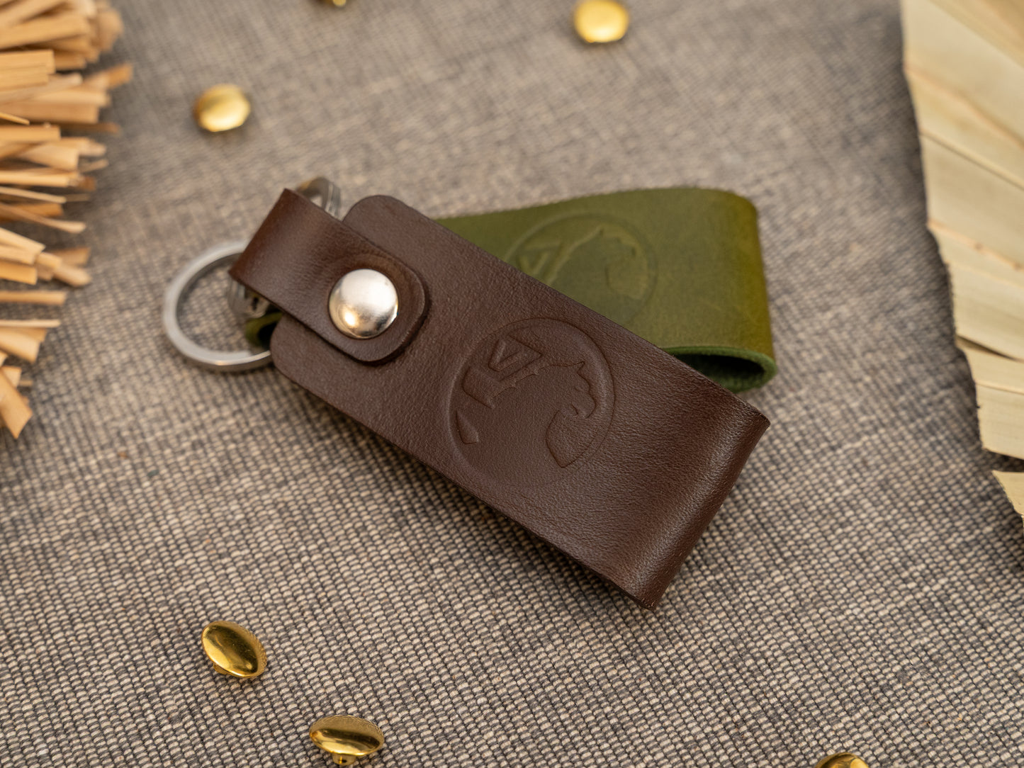 Folded dark brown and olive green leather keyrings/keychains with the Vauxhall car logo debossed on them. Made from full grain leather with stainless steel split ring and rivet.