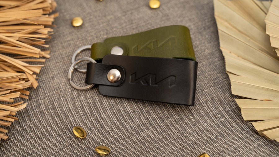 Folded black and olive green leather keyrings/keychains with the Kia car logo debossed on them. Made from full grain leather with stainless steel split ring and rivet.