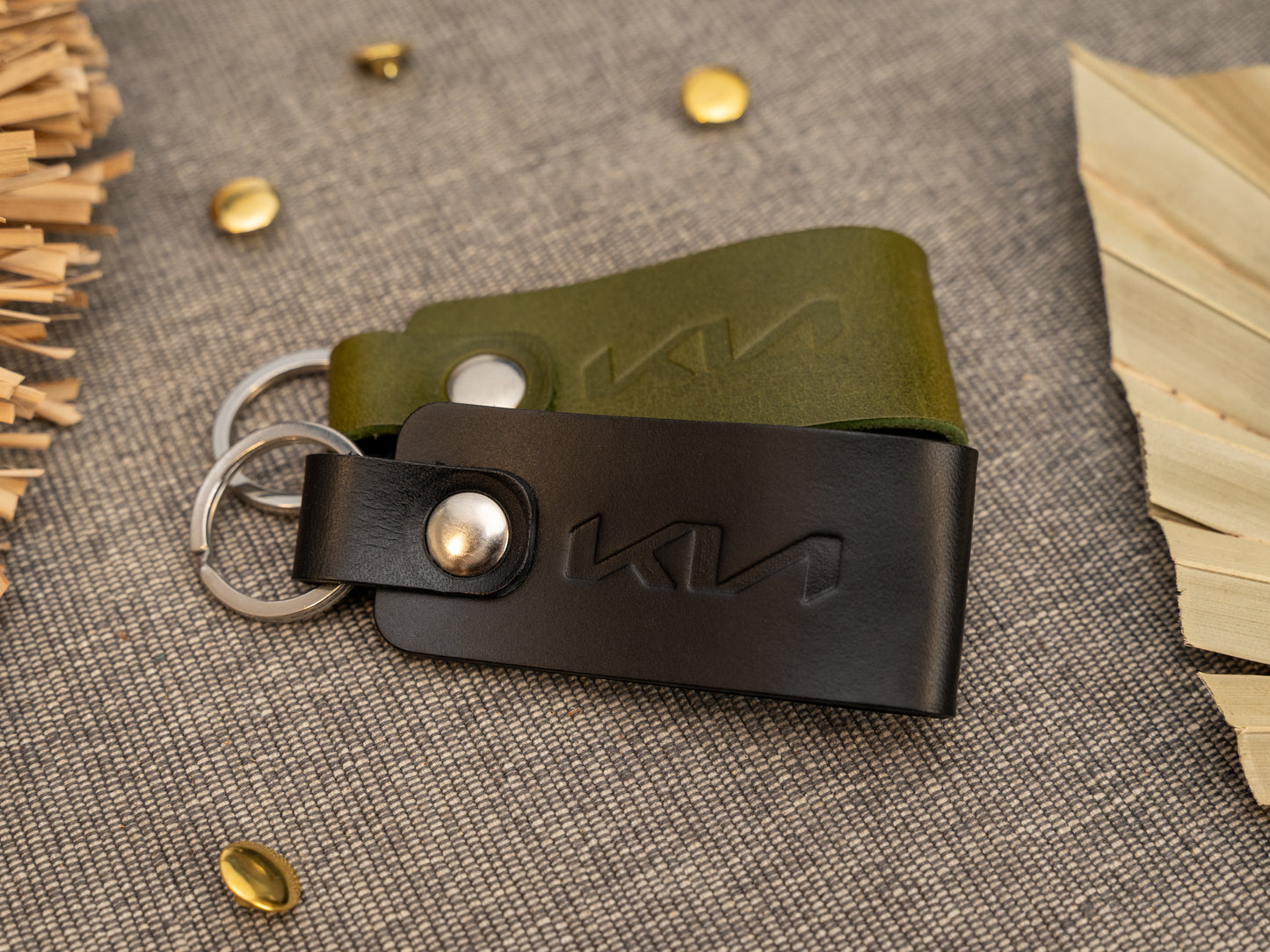 Folded black and olive green leather keyrings/keychains with the Kia car logo debossed on them. Made from full grain leather with stainless steel split ring and rivet.