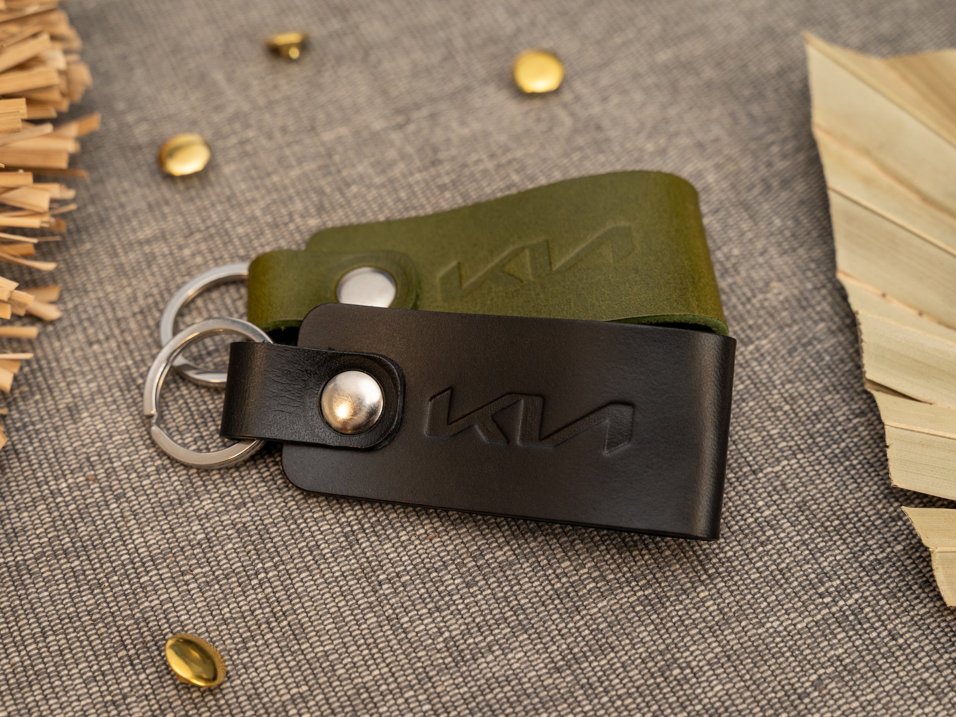 Folded black and olive green leather keyrings/keychains with the Kia car logo debossed on them. Made from full grain leather with stainless steel split ring and rivet.