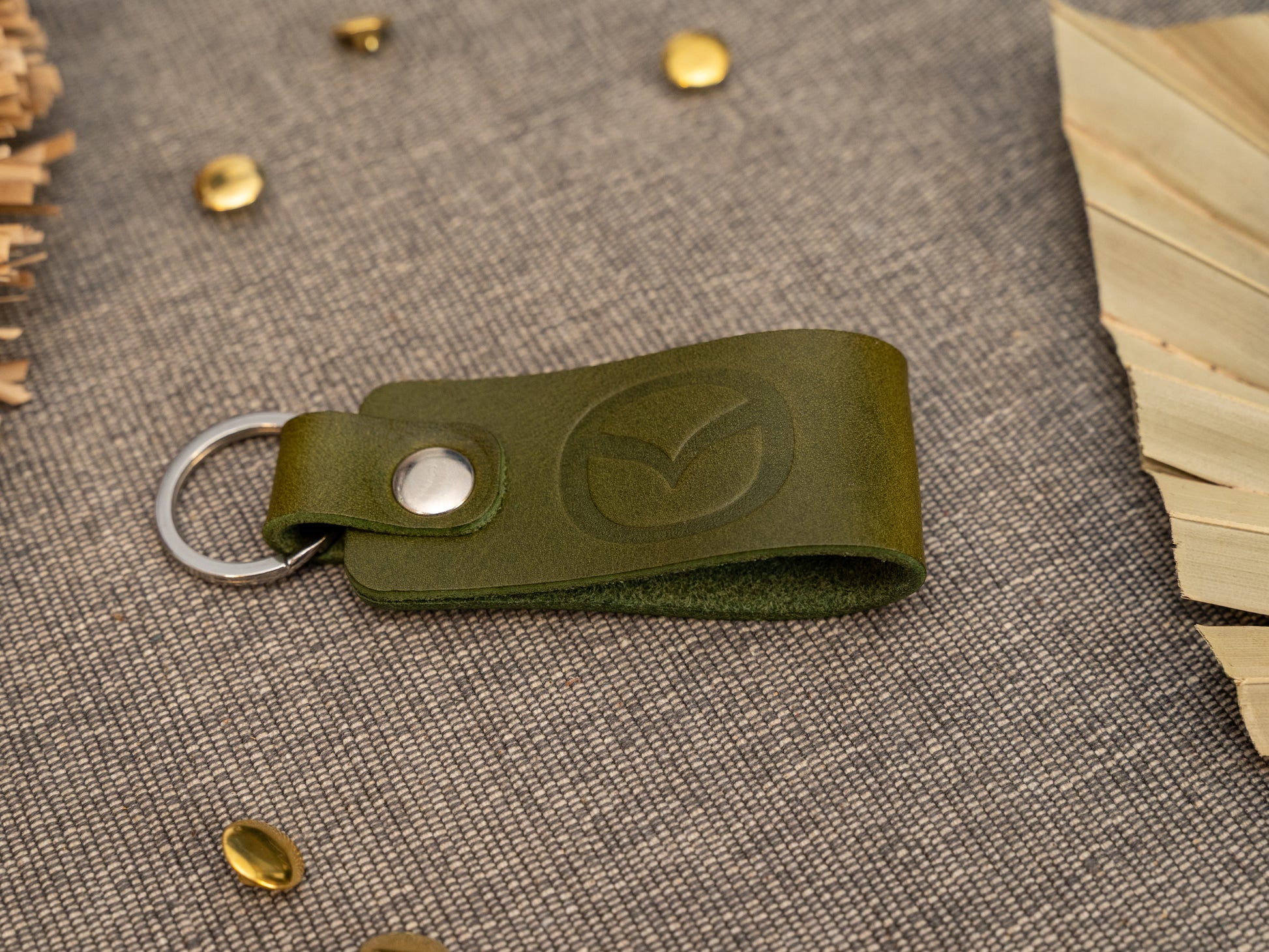 Folded olive green leather keyring/keychain with the Mazda car logo debossed on it. Made from full grain leather with stainless steel split ring and rivet.