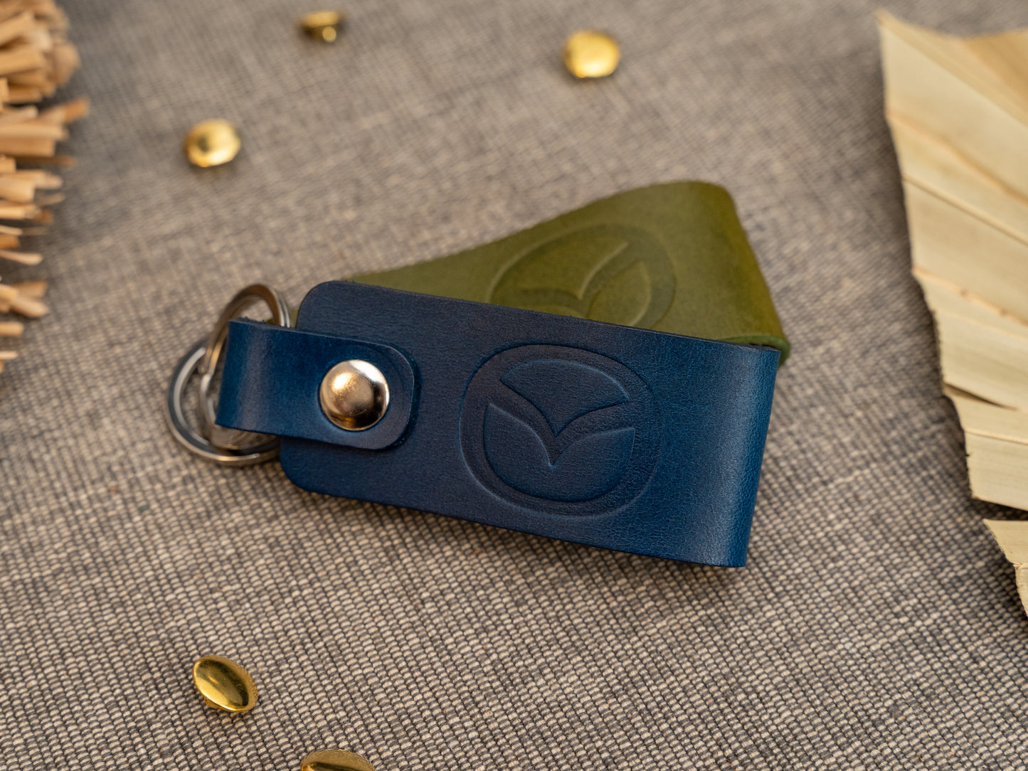 Folded navy blue and olive green leather keyrings/keychains with the Mazda car logo debossed on them. Made from full grain leather with stainless steel split ring and rivet.