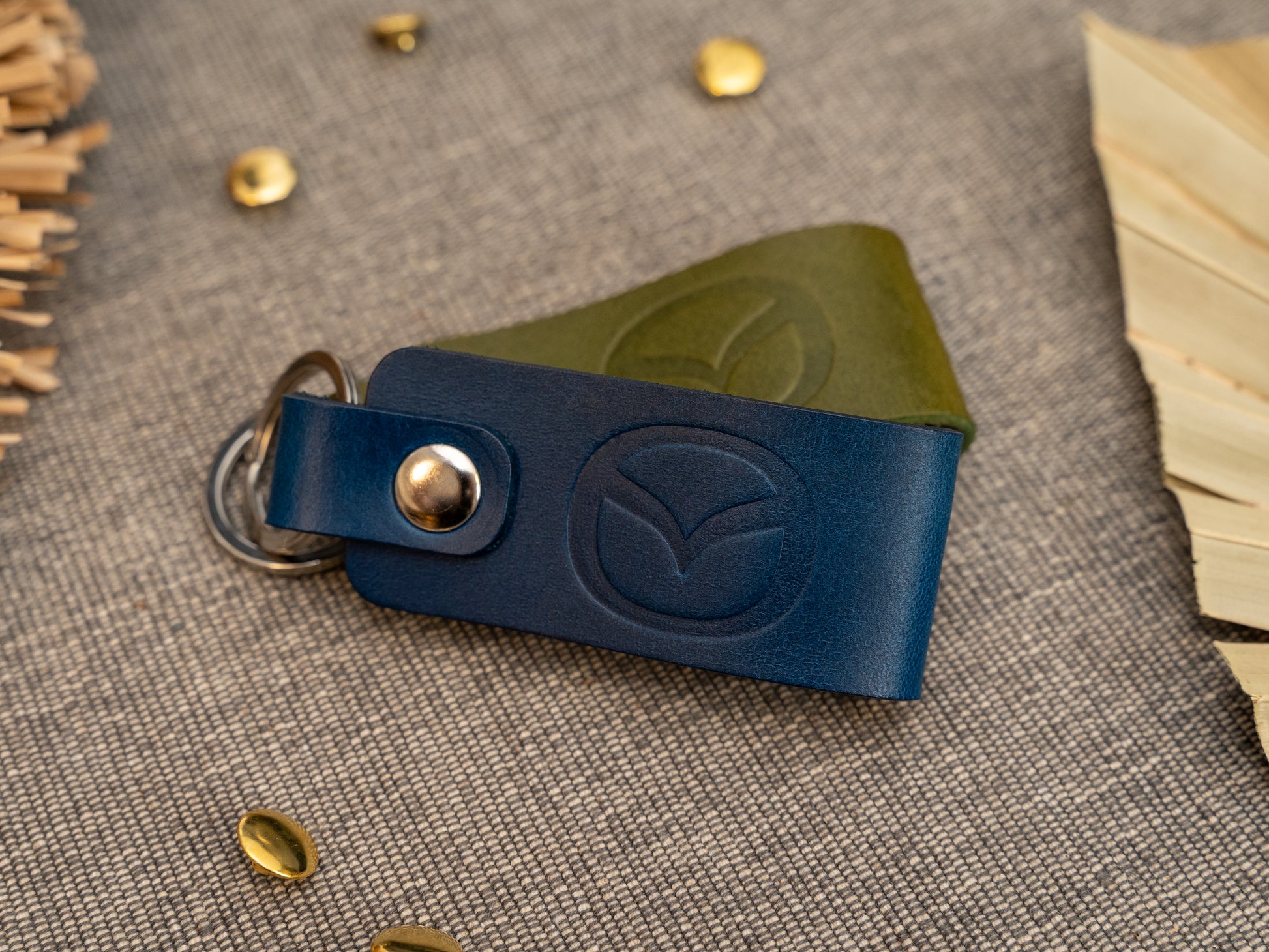 Folded navy blue and olive green leather keyrings/keychains with the Mazda car logo debossed on them. Made from full grain leather with stainless steel split ring and rivet.