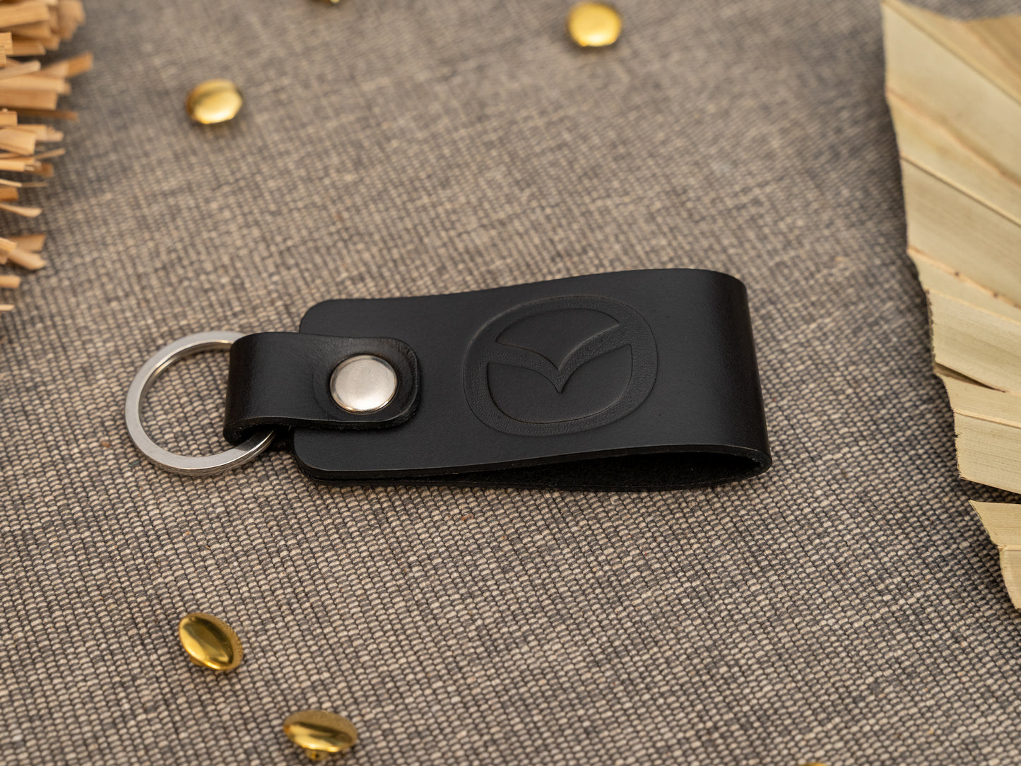 Folded black leather keyring/keychain with the Mazda car logo debossed on it. Made from full grain leather with stainless steel split ring and rivet.
