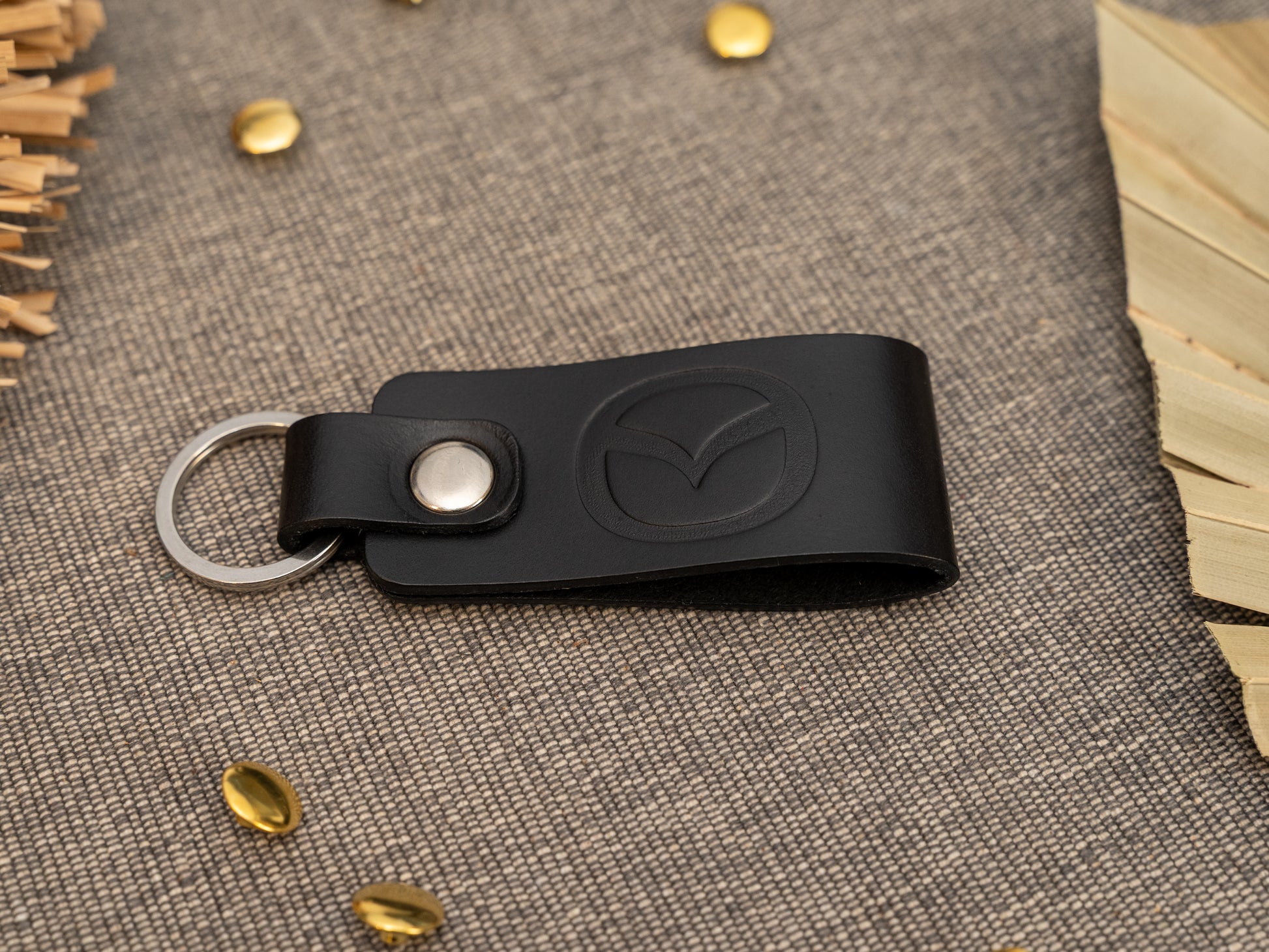 Folded black leather keyring/keychain with the Mazda car logo debossed on it. Made from full grain leather with stainless steel split ring and rivet.